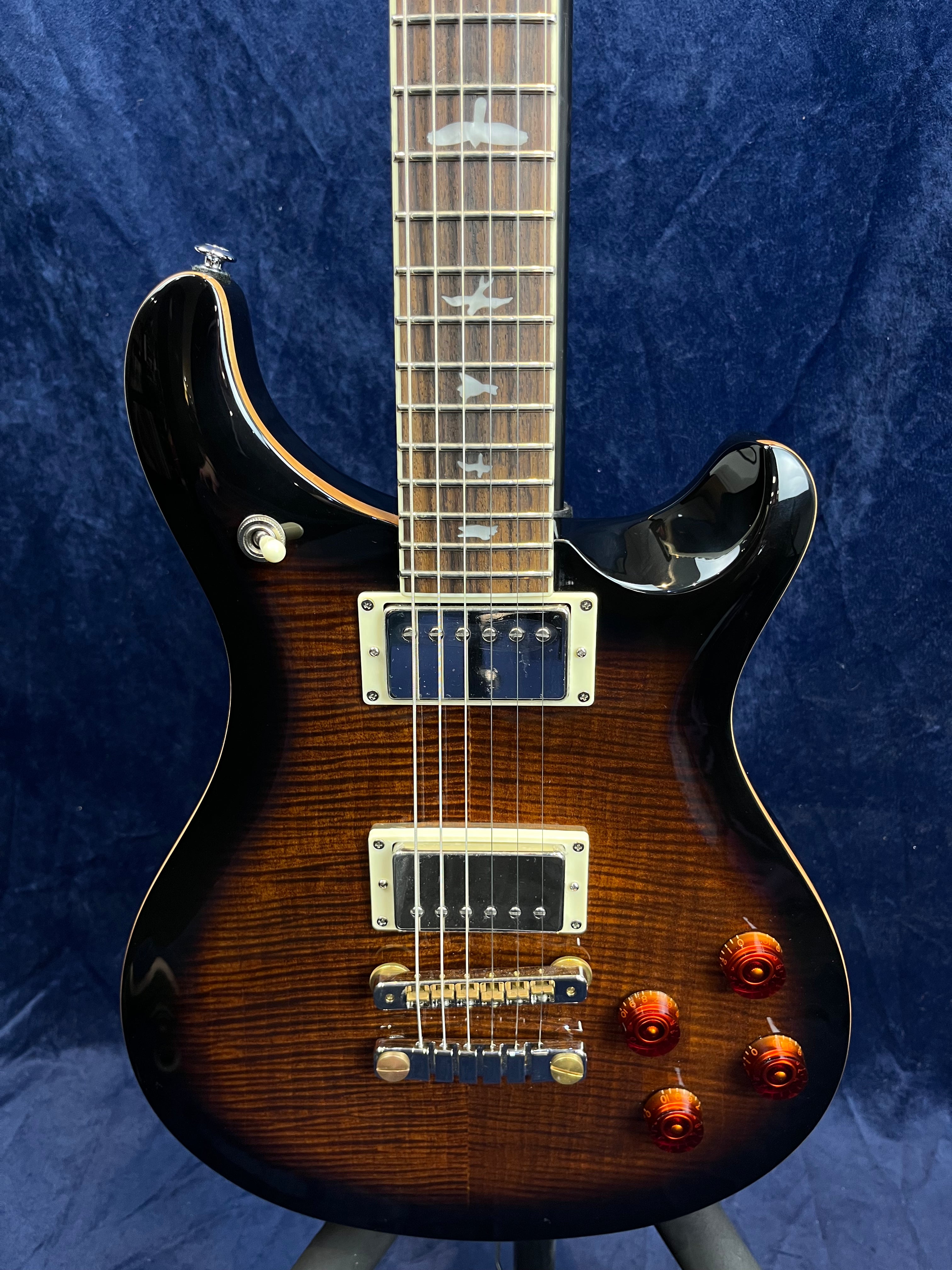 Electric guitar with a brown sunburst finish, two humbucker pickups, four amber control knobs, and bird-shaped inlays on the fretboard.