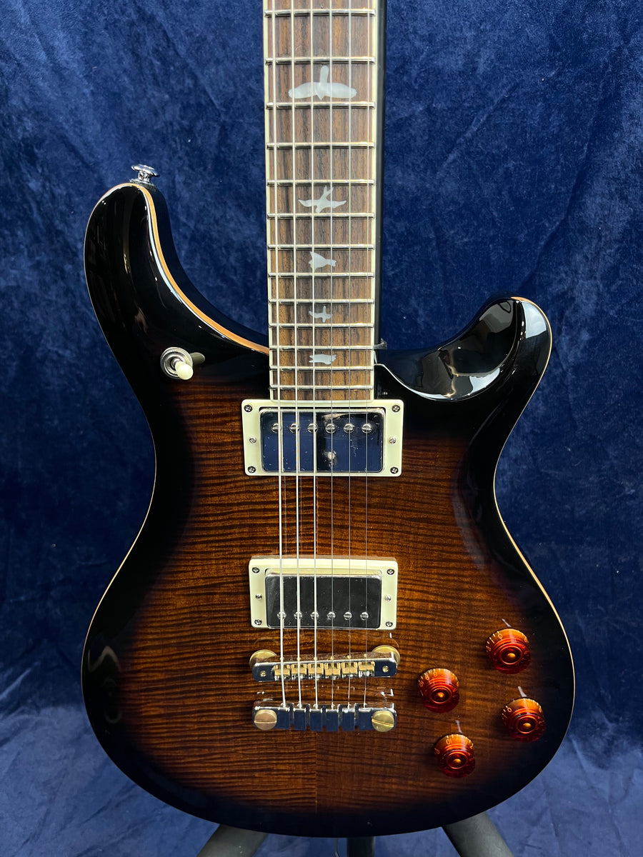 Electric guitar with a brown sunburst finish, two humbucker pickups, four amber control knobs, and bird-shaped inlays on the fretboard.
