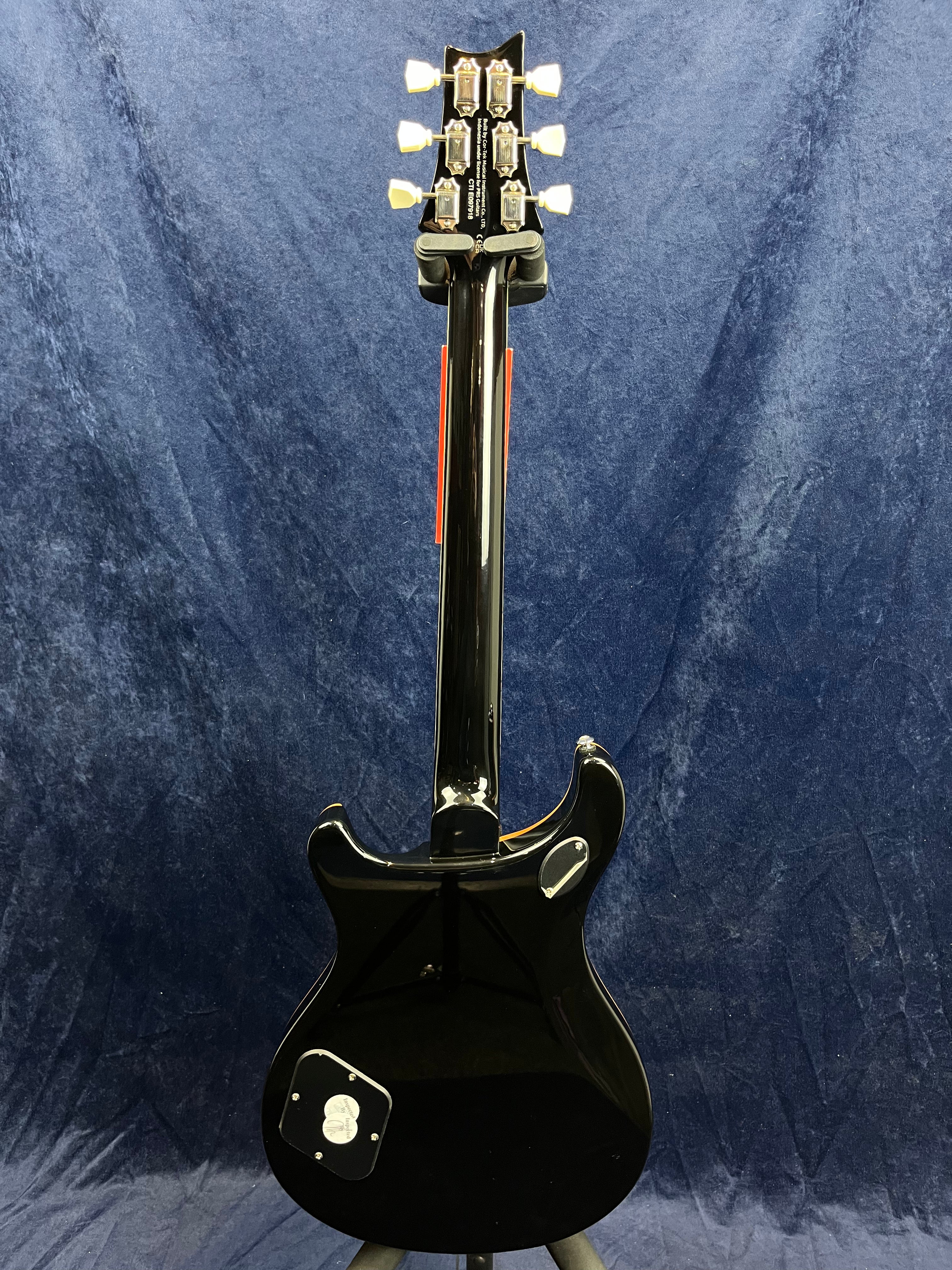 Glossy black electric guitar seen from the back, showing six tuning pegs, two cover plates on the body, and a curved, double-cutaway shape.