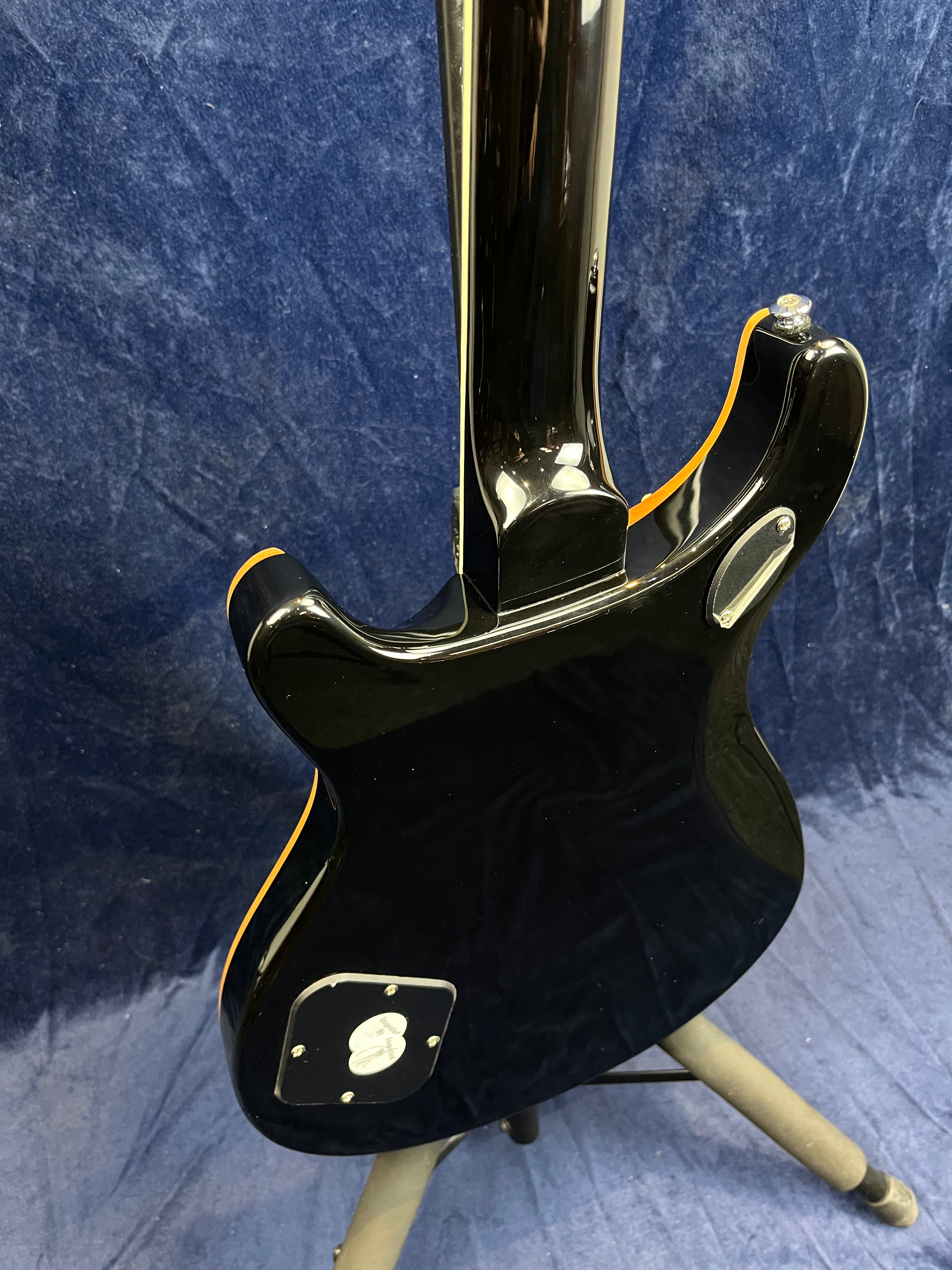 Glossy black electric guitar shown from the back, with cream binding, mounted on a stand against a dark blue textured background.