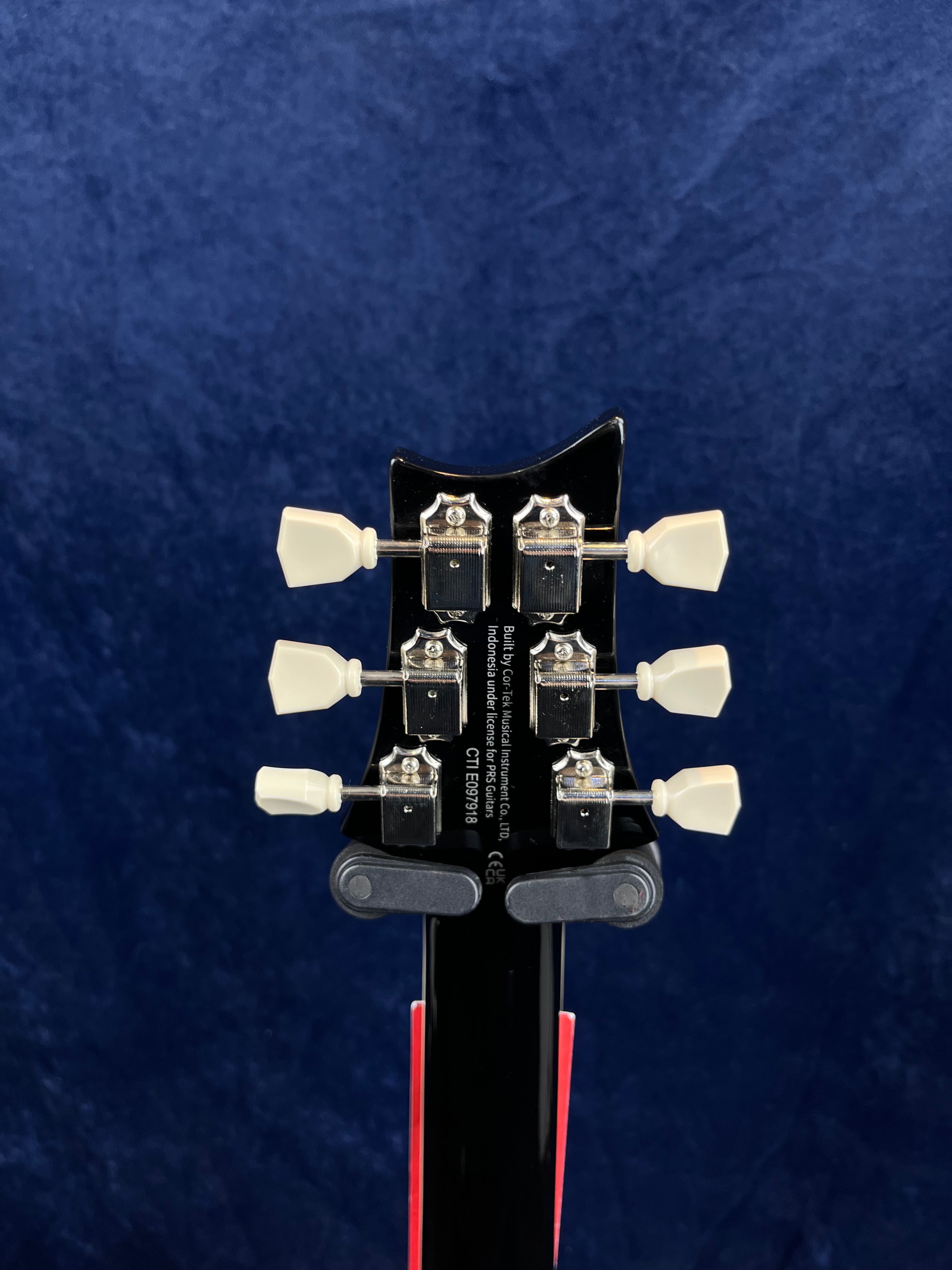 Six cream tuning pegs and chrome tuners on the back of a black electric guitar headstock, serial number and manufacturer info in white text.