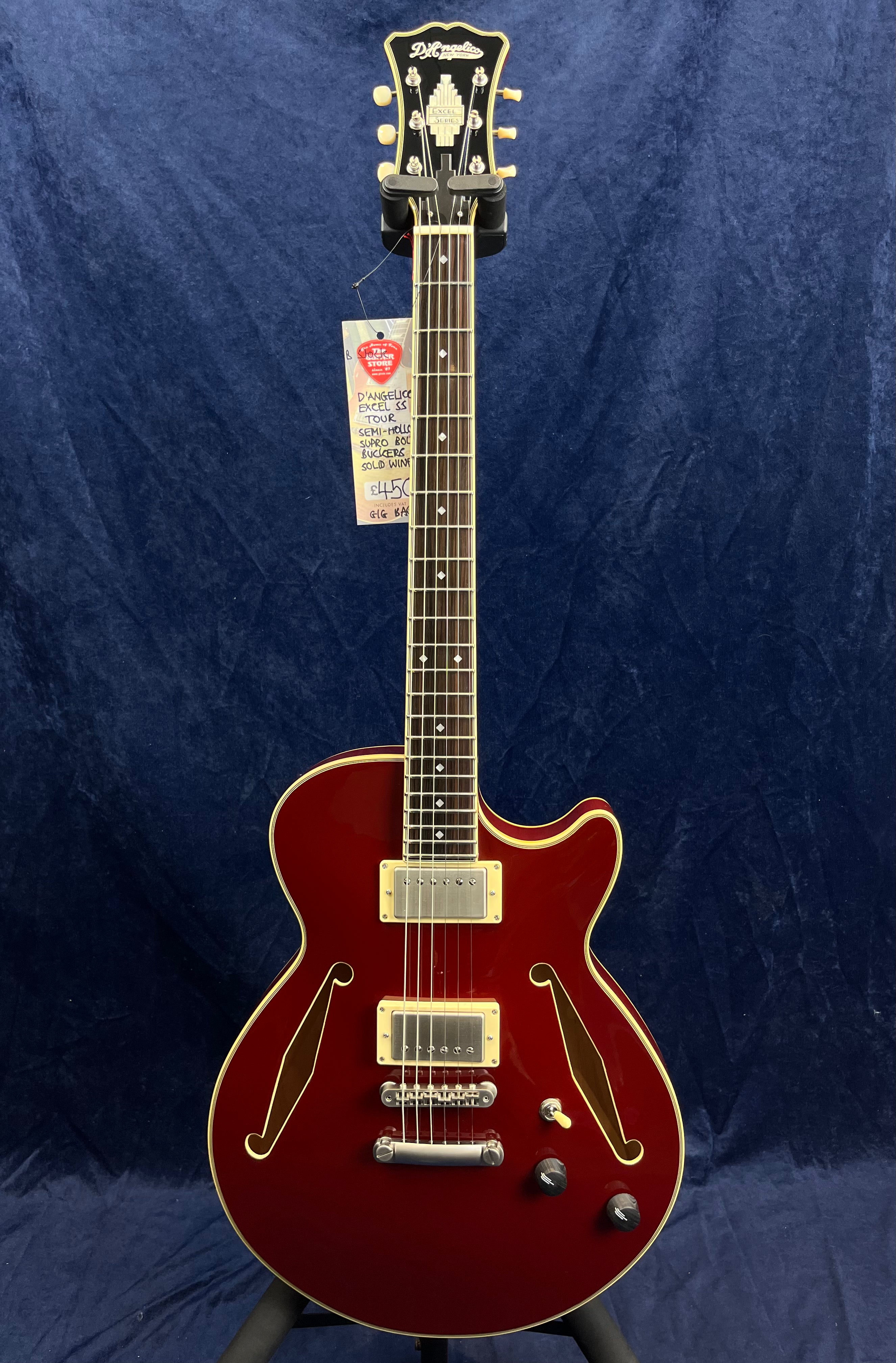 Red semi-hollow electric guitar with gold hardware, two pickups, double f-holes, and three control knobs, displayed upright against a dark blue background.