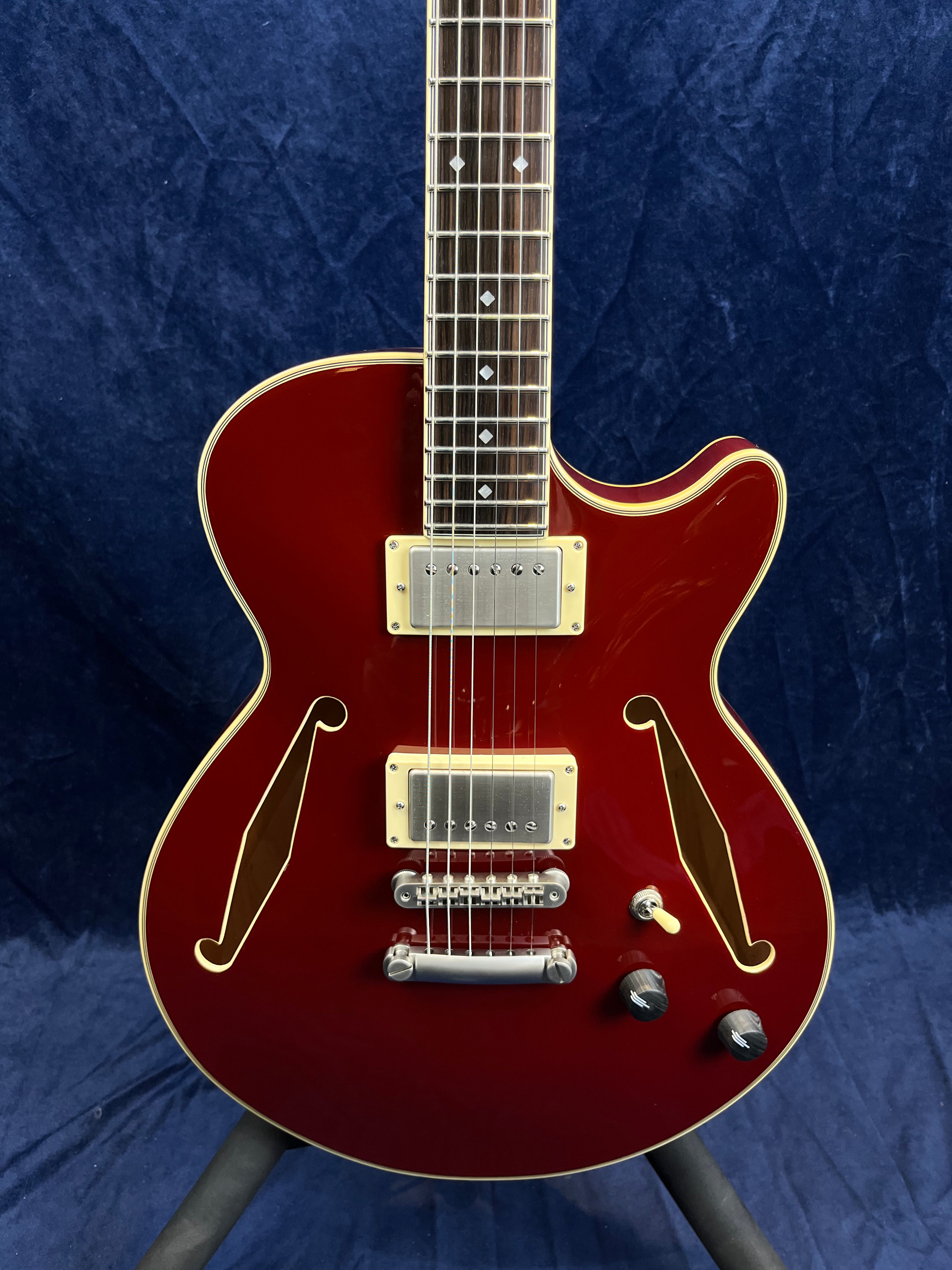 Red semi-hollow electric guitar with gold-edged body, two humbucker pickups, F-holes, three control knobs, and a toggle switch.