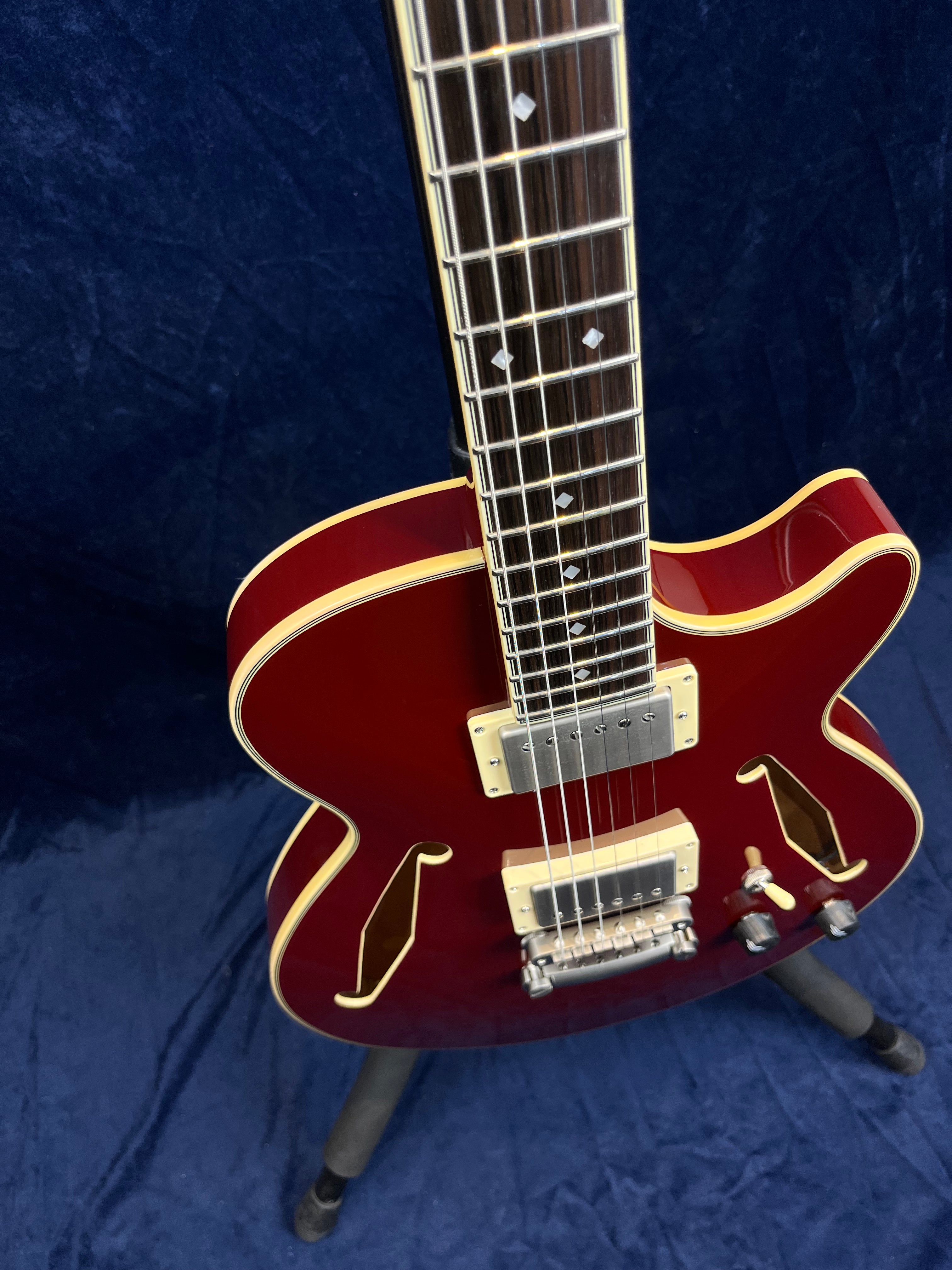 Cherry red semi-hollow electric guitar with cream binding, chrome humbucker pickups, gold f-hole accents, and two control knobs.