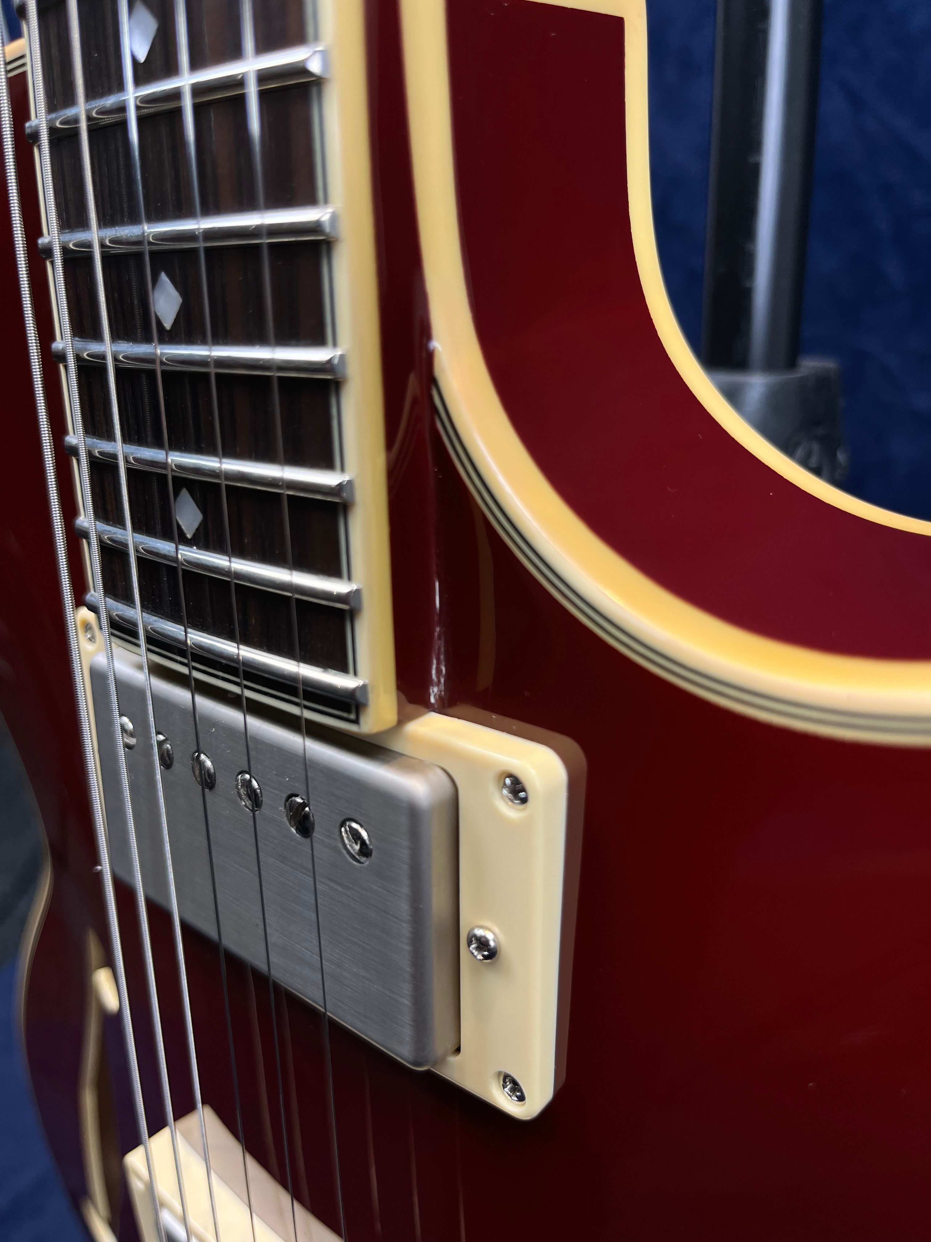 Close-up of an electric guitar showing a red body with cream binding, a metal humbucker pickup, and part of the fretboard with pearl inlays.