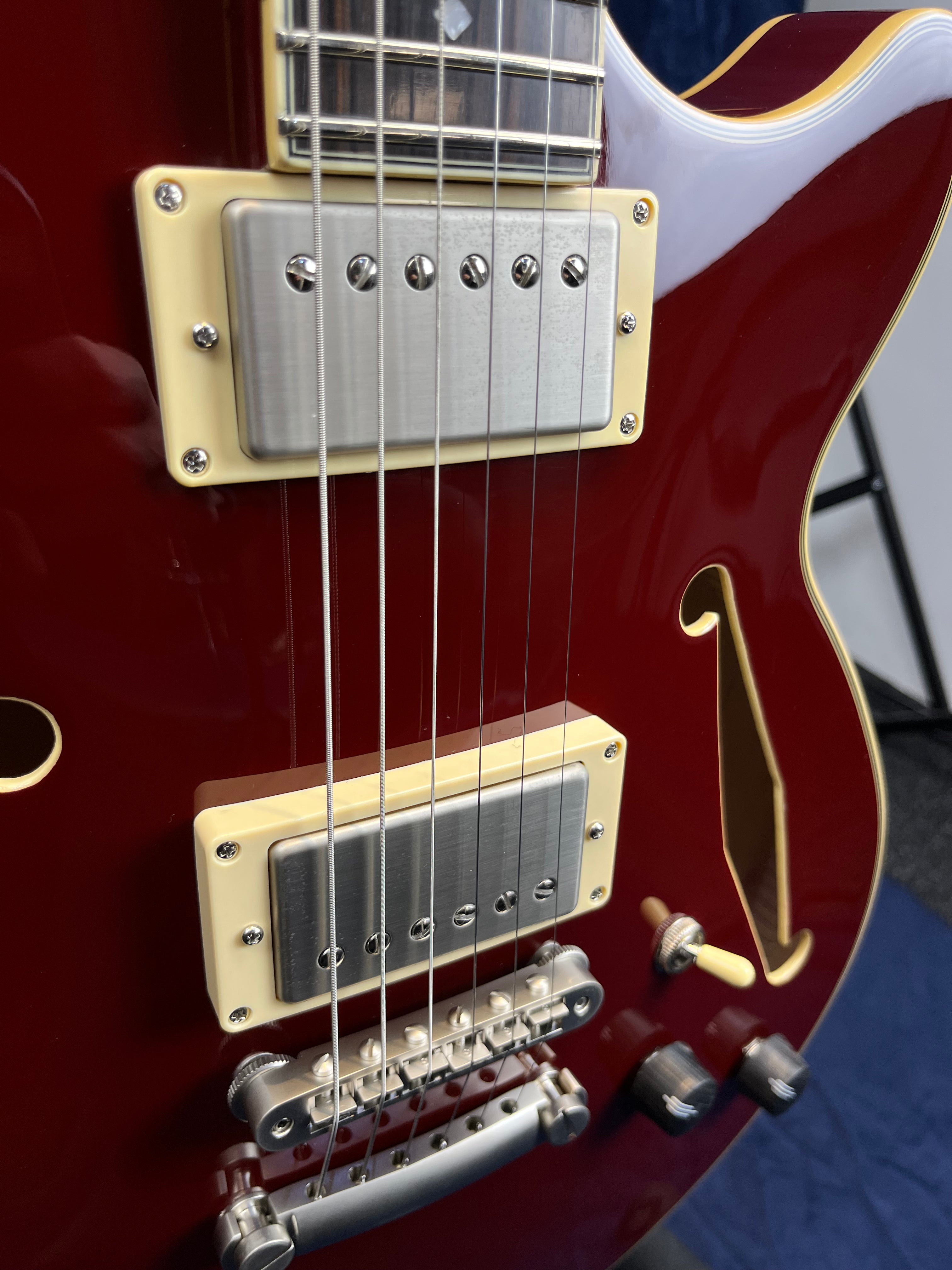 Red semi-hollow electric guitar body with two chrome humbucker pickups, cream pickup rings, four control knobs, and an f-shaped sound hole.