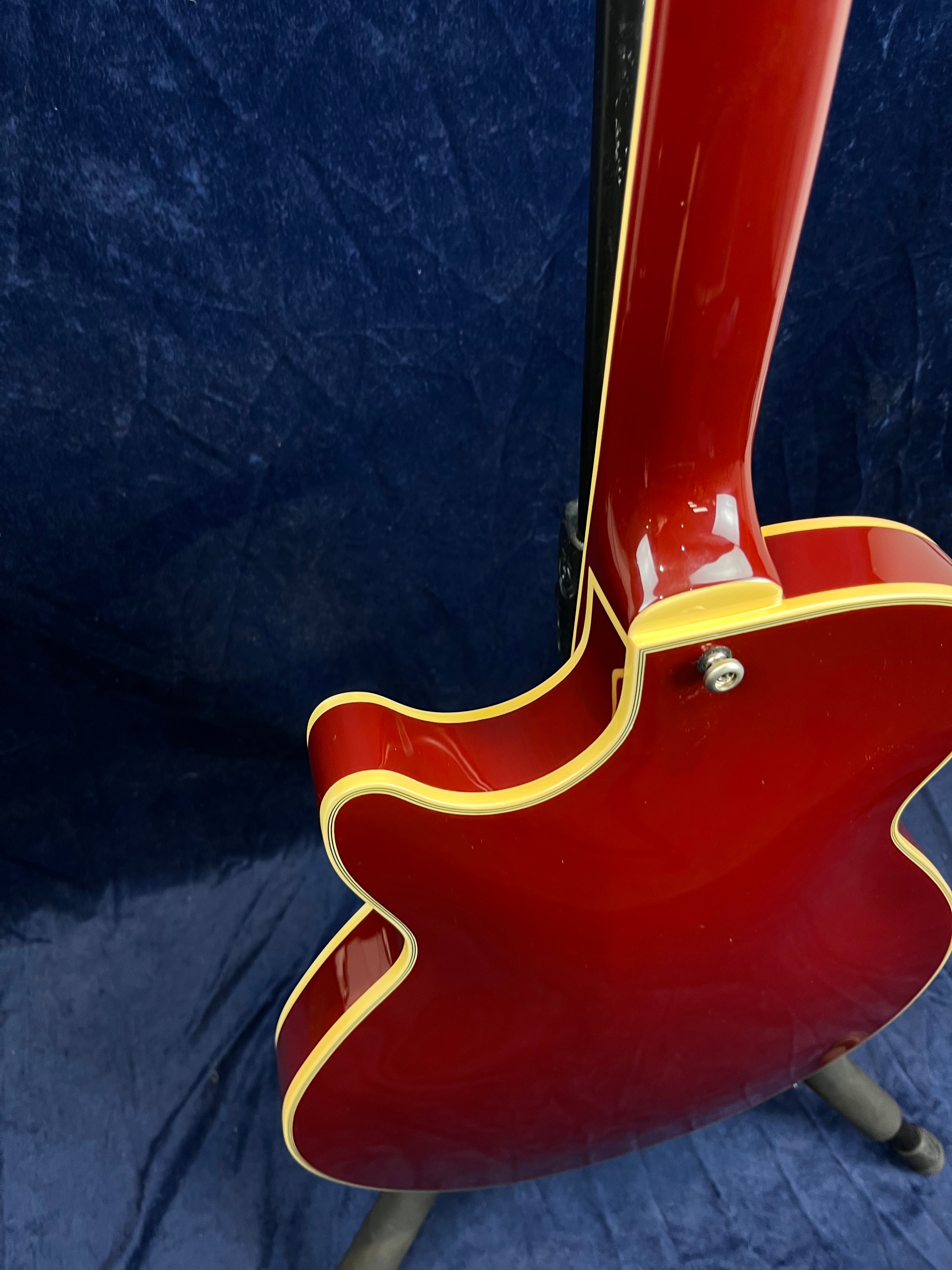 Red electric guitar with a vintage-style double cutaway body, cream binding along the edges, photographed from the back against a dark blue background.