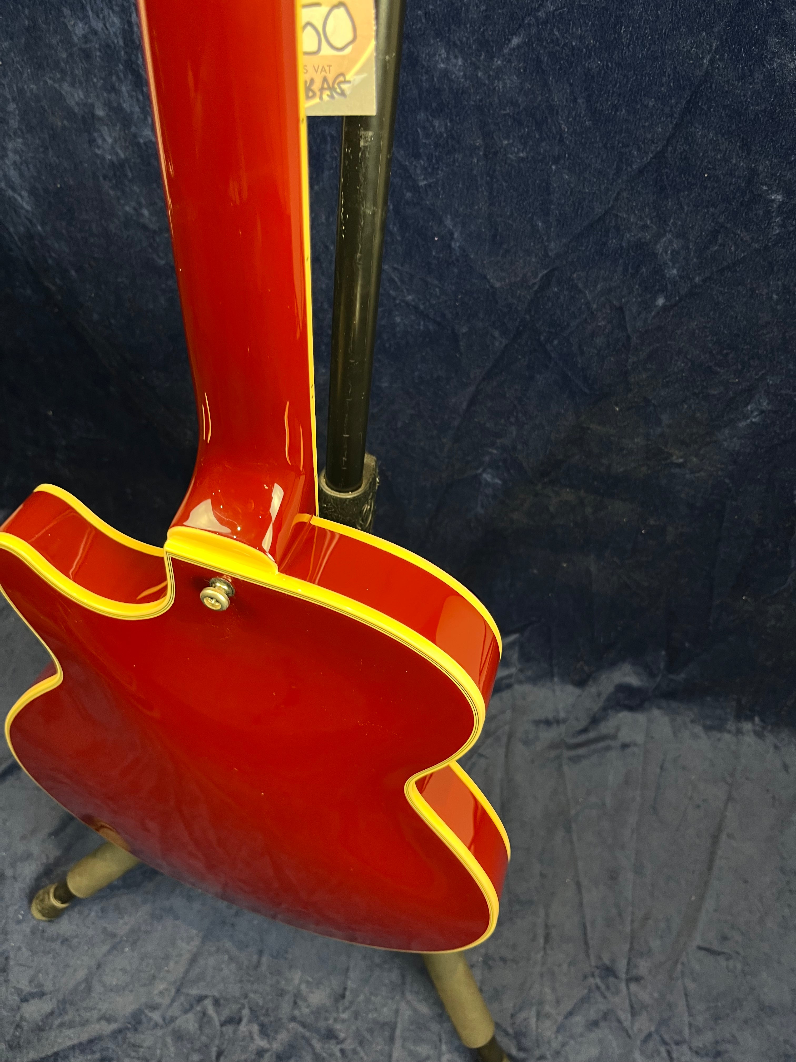 Glossy red electric guitar with yellow edge binding, shown from the back while resting on a stand against a dark blue background.
