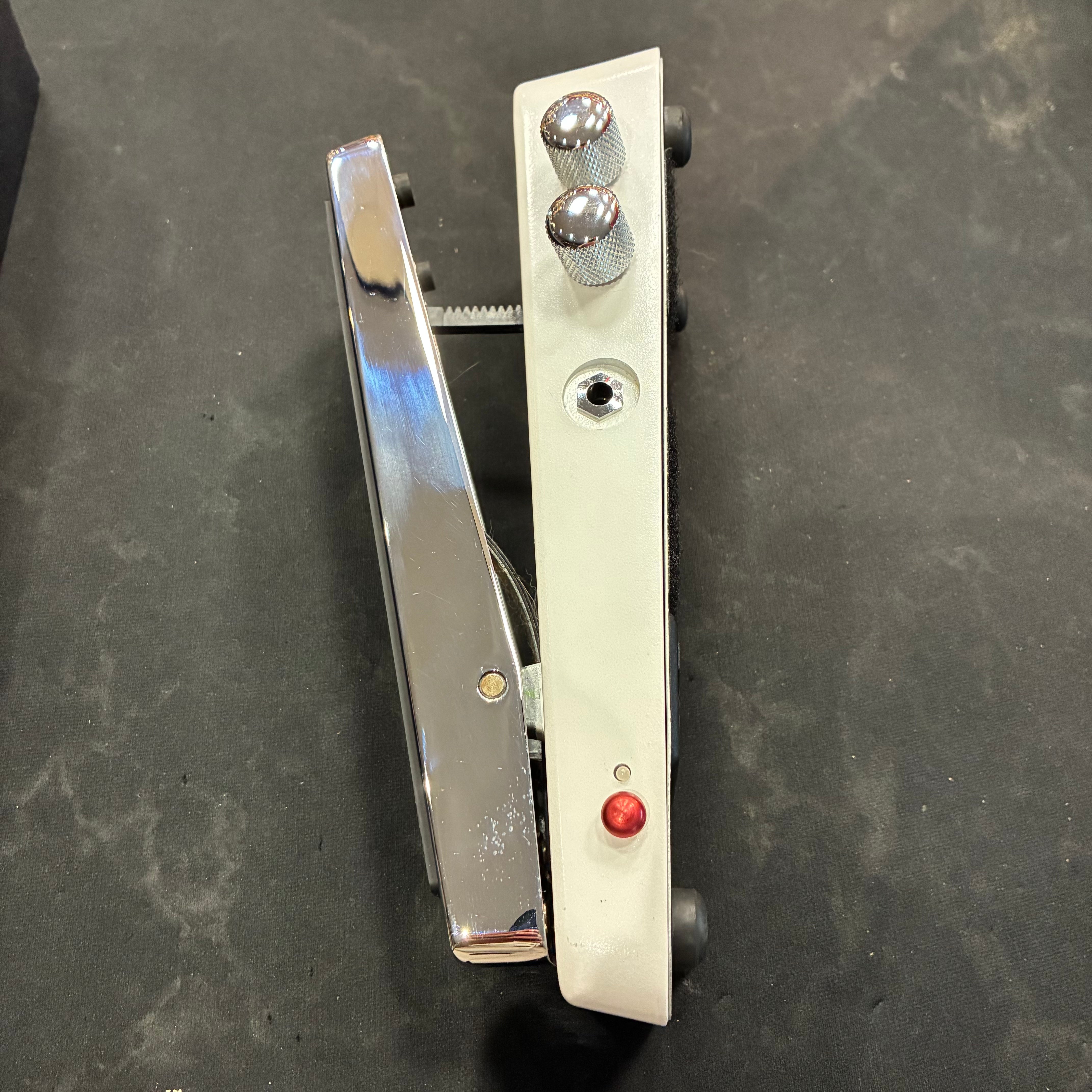 Silver FX pedal with a treadle, two metal knobs, a red LED, and an input jack on a black surface.