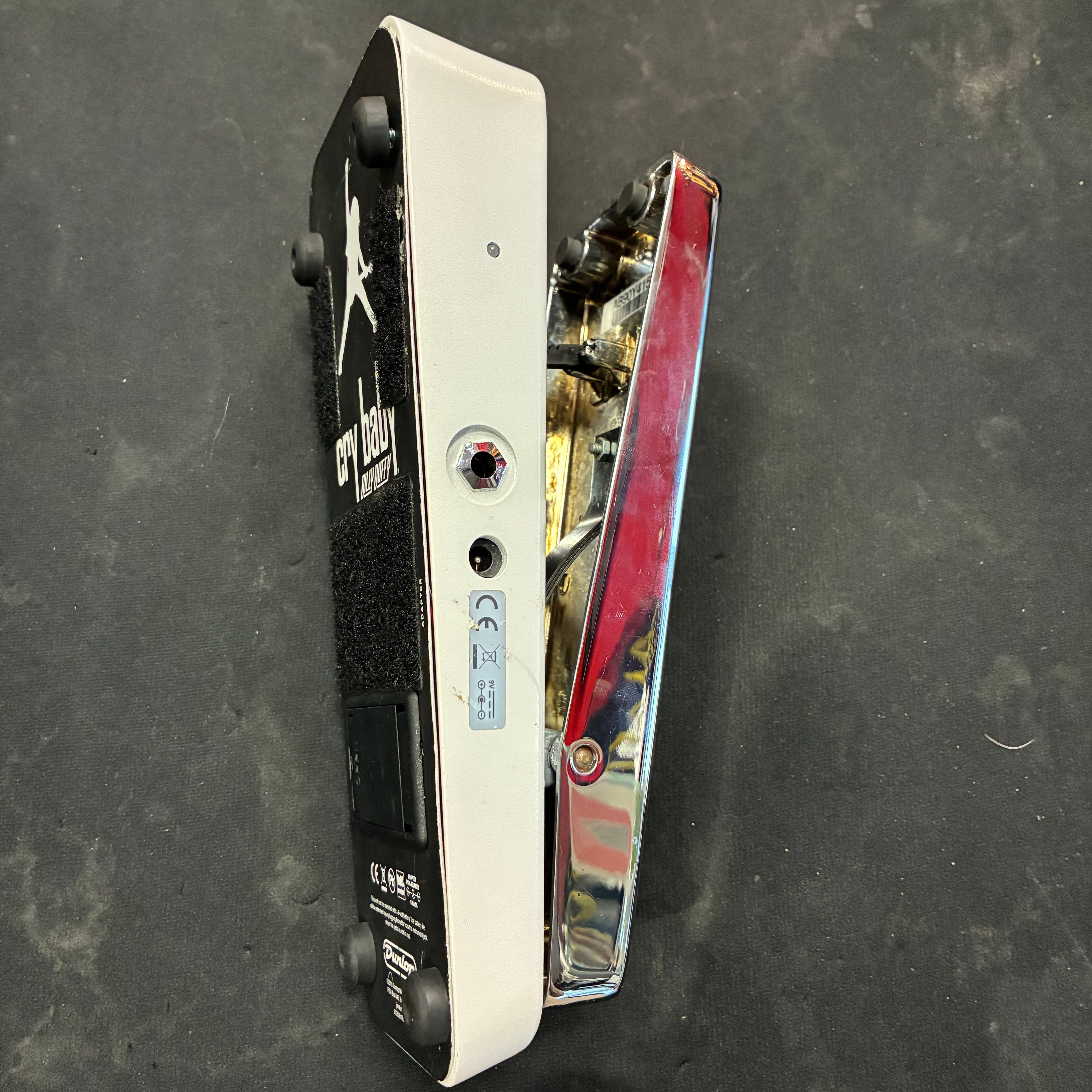 White and chrome Cry Baby Wah FX pedal, side view, with black rubber feet, input jack, and textured foot grip; placed on a dark surface.