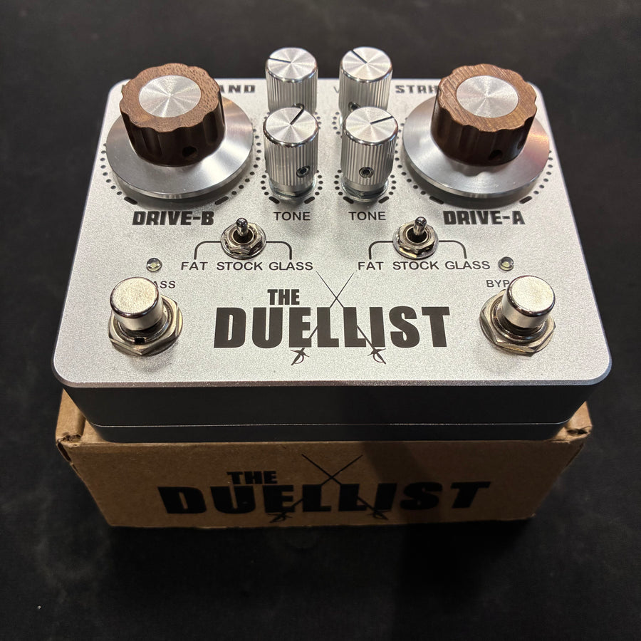 Guitar FX pedal named The Duellist, featuring two large brown knobs, four silver knobs, two metal switches, and two footswitches on a silver casing.