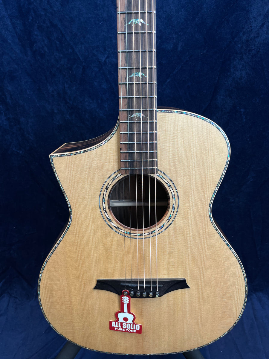 Natural wood acoustic guitar with light finish, decorative inlays on the neck, and a sticker near the bridge reading "ALL SOLID PURE TONE."
