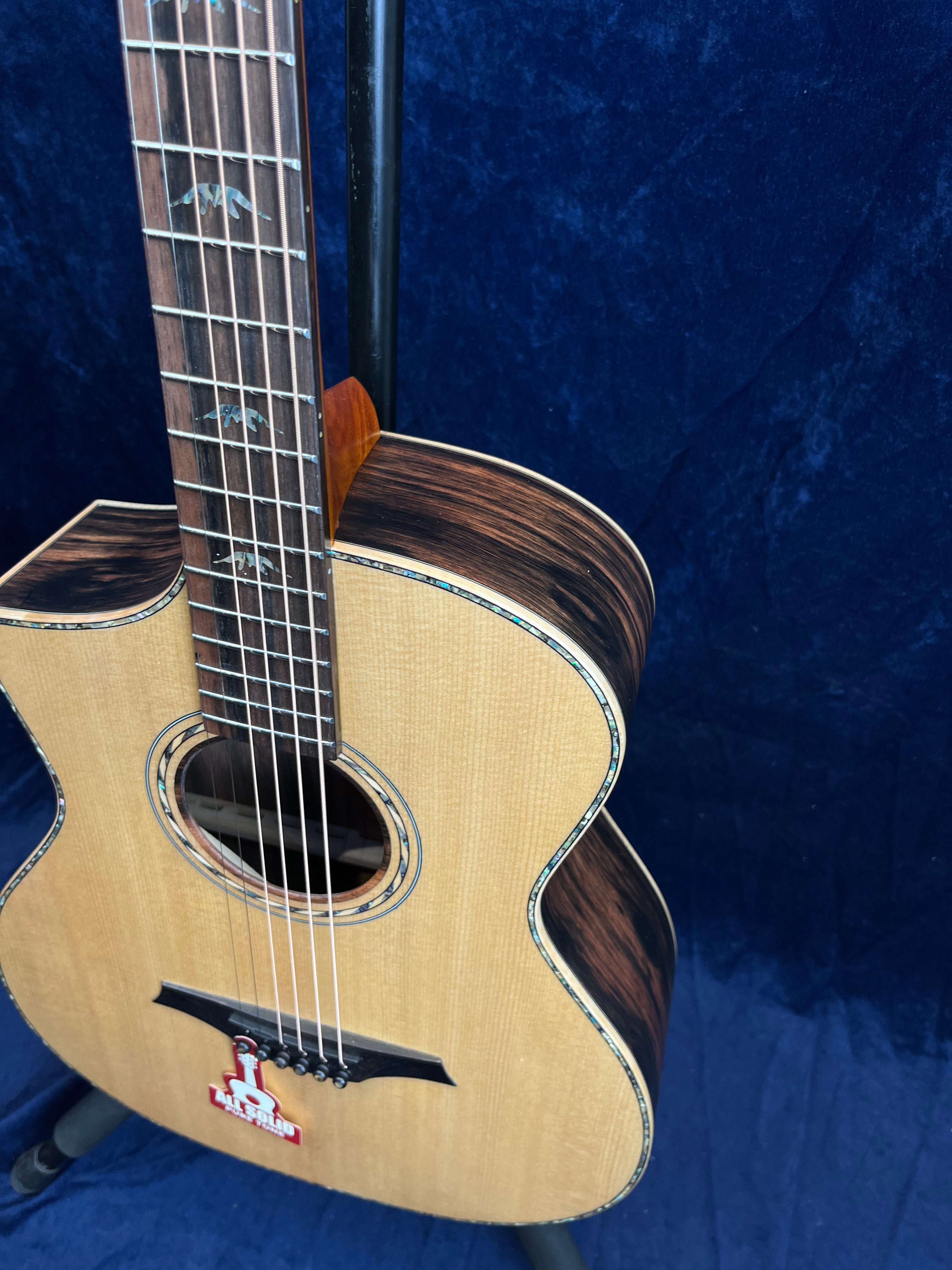 Light wood acoustic guitar with dark wood sides, decorative inlays on the fretboard, and a red "all solid" tag on the lower body.