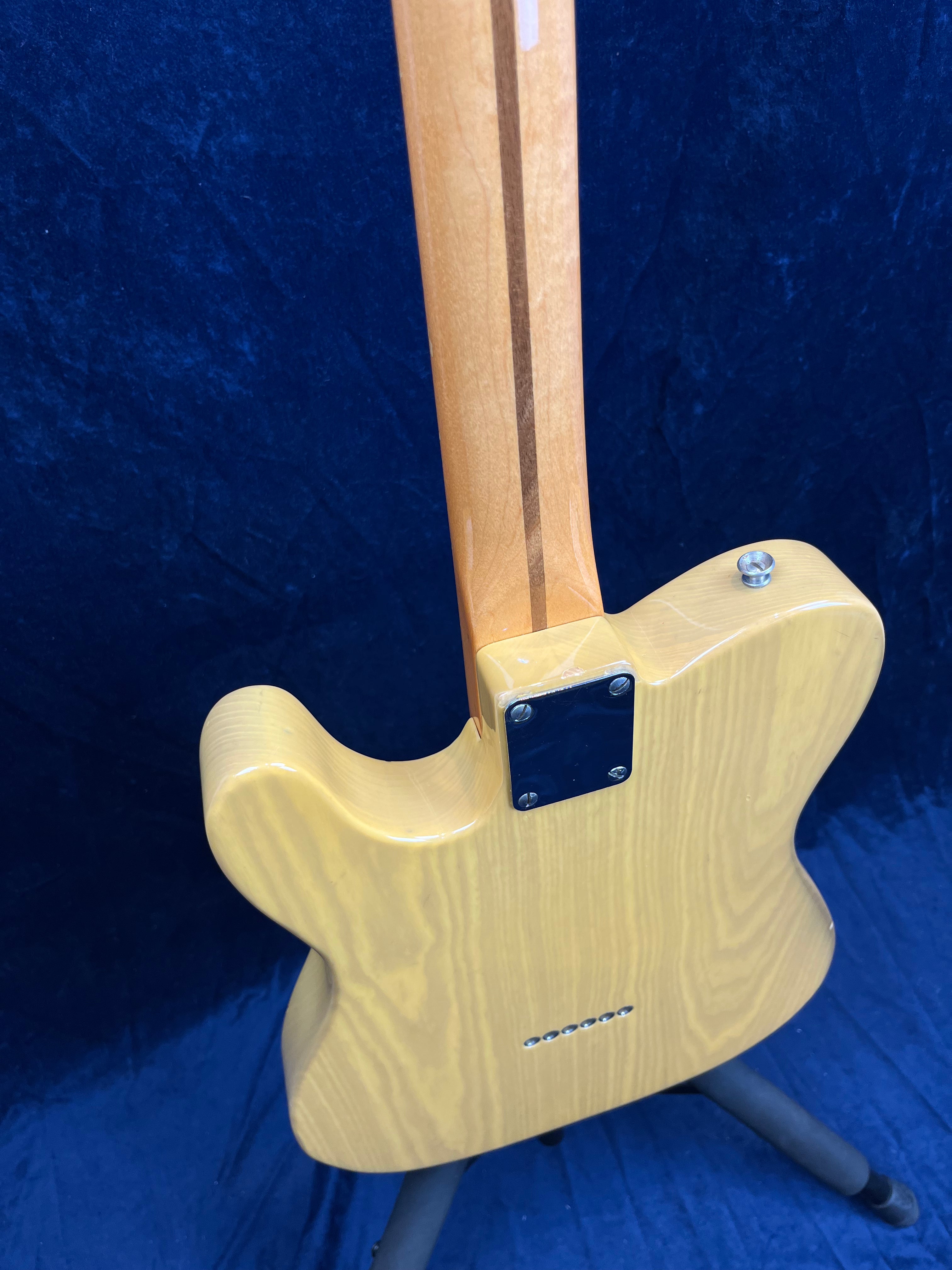 Light-colored solid-body electric guitar shown from the back, with a natural wood finish and a neck featuring a contrasting central stripe.