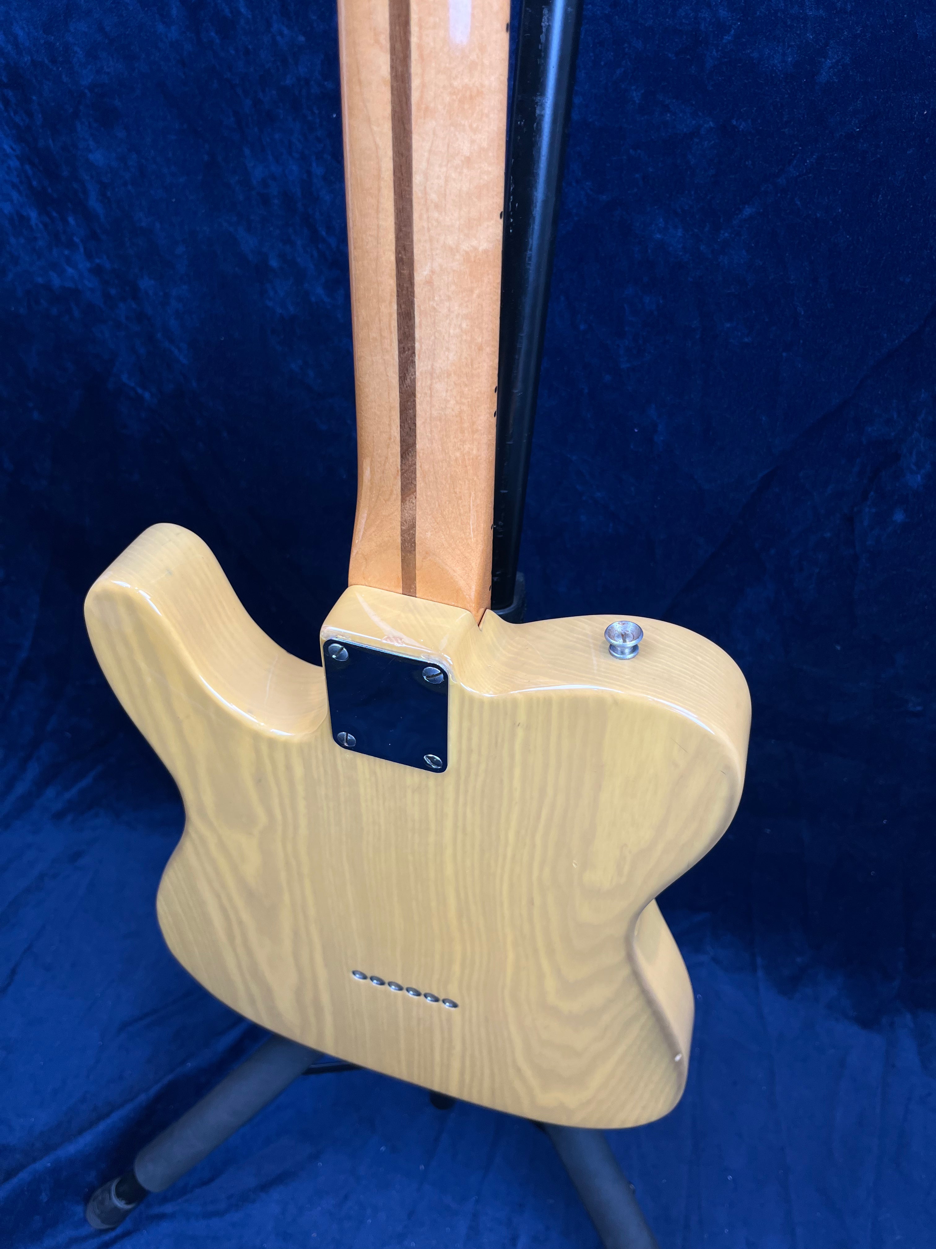 Natural wood finish electric guitar viewed from the back, showing the neck joint, metal neck plate, and wood grain pattern on the body.