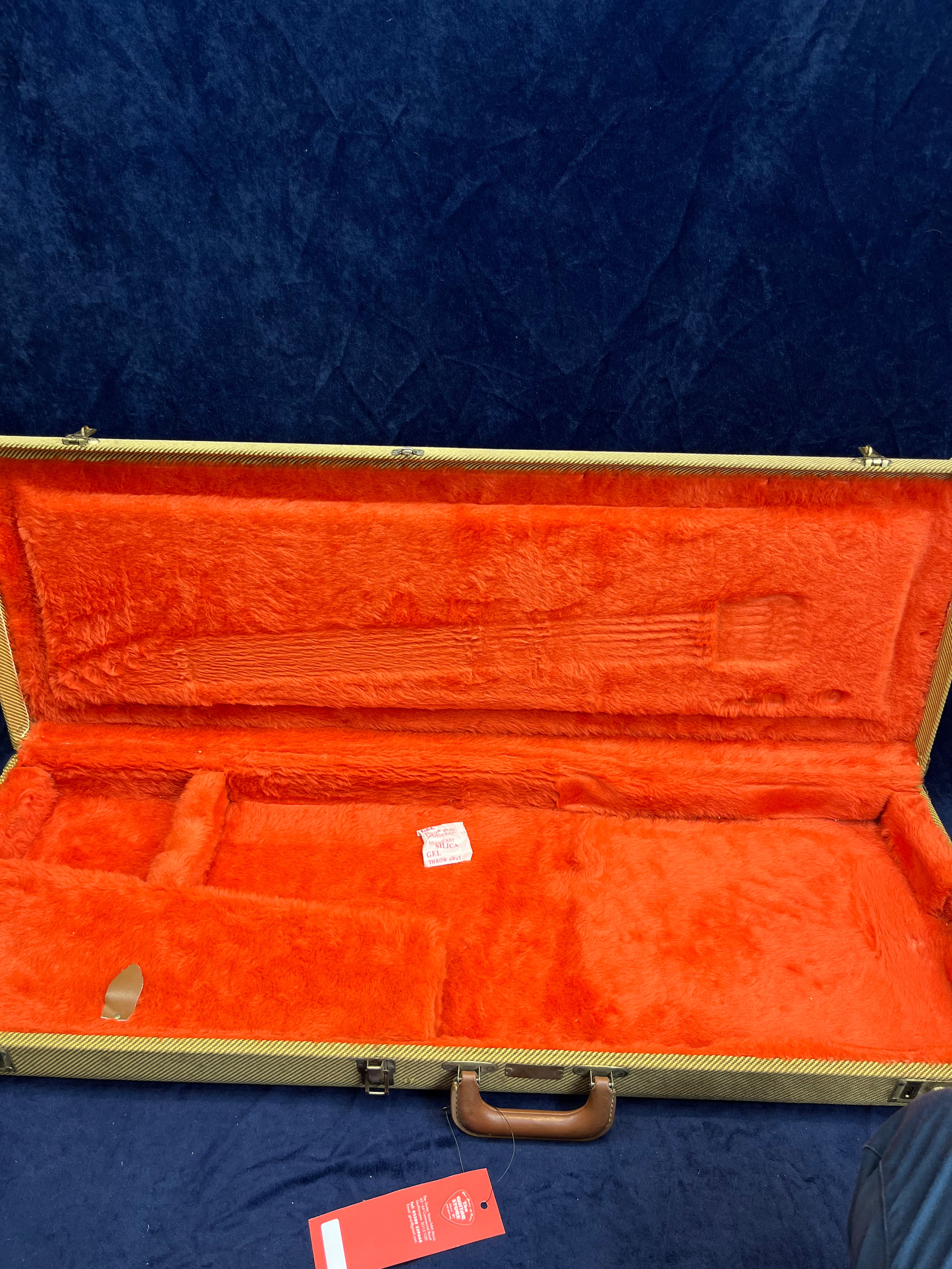 Empty electric guitar case lined with bright orange plush fabric, compartments for accessories, and a brown handle at the front.