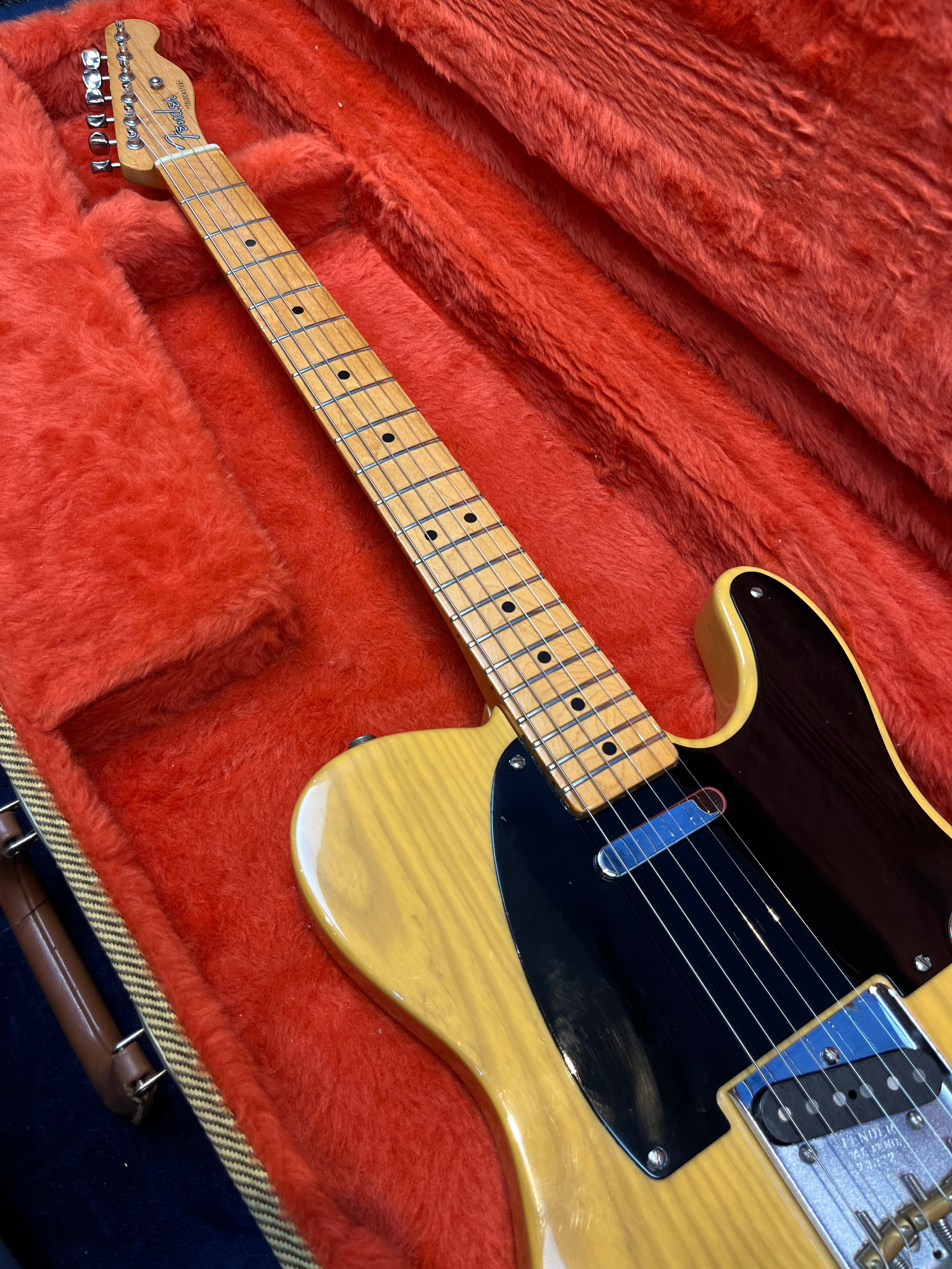 Blonde electric guitar with black pickguard in a red plush-lined hard case. Maple neck with dot inlays, single-coil pickups, classic Telecaster shape.