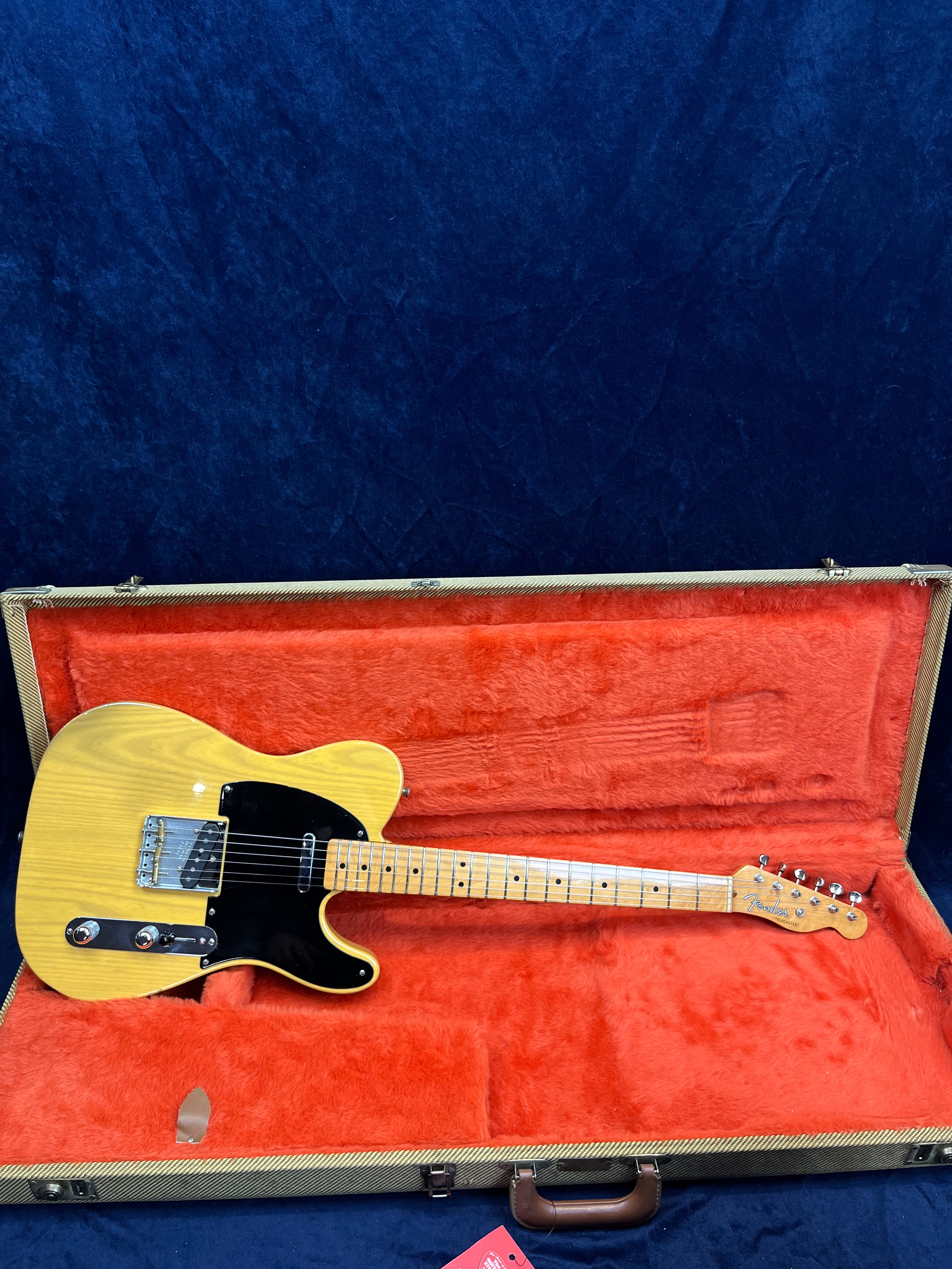 Natural wood finish electric guitar with black pickguard, single-cutaway body, maple neck, in an open orange-lined hard case.