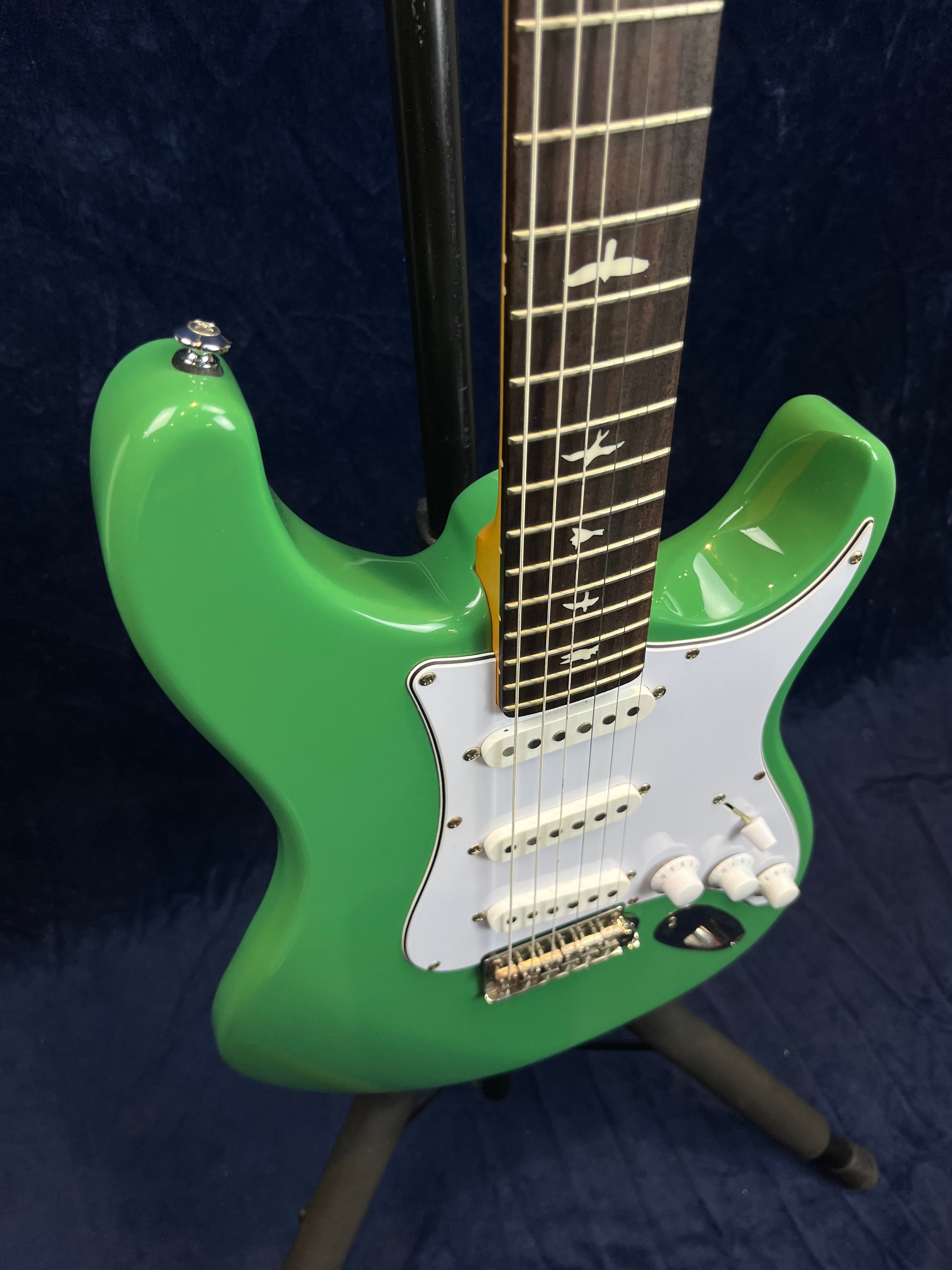 Green electric guitar with a white pickguard, three white single-coil pickups, three white knobs, and bird inlays on the fretboard.