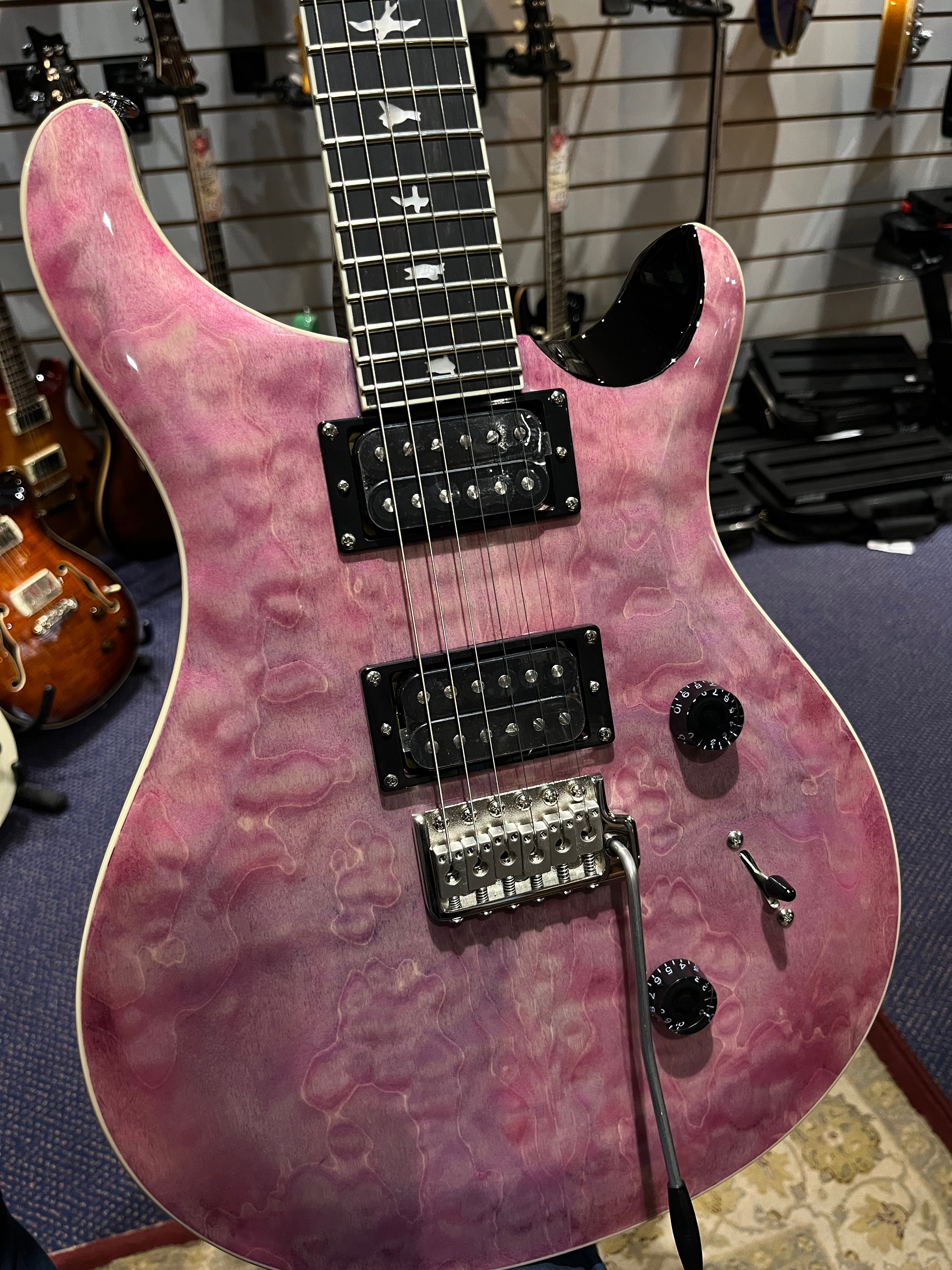 Purple-pink electric guitar with quilted finish, black pickups, bird inlays on the fretboard, two control knobs, and a tremolo bridge.