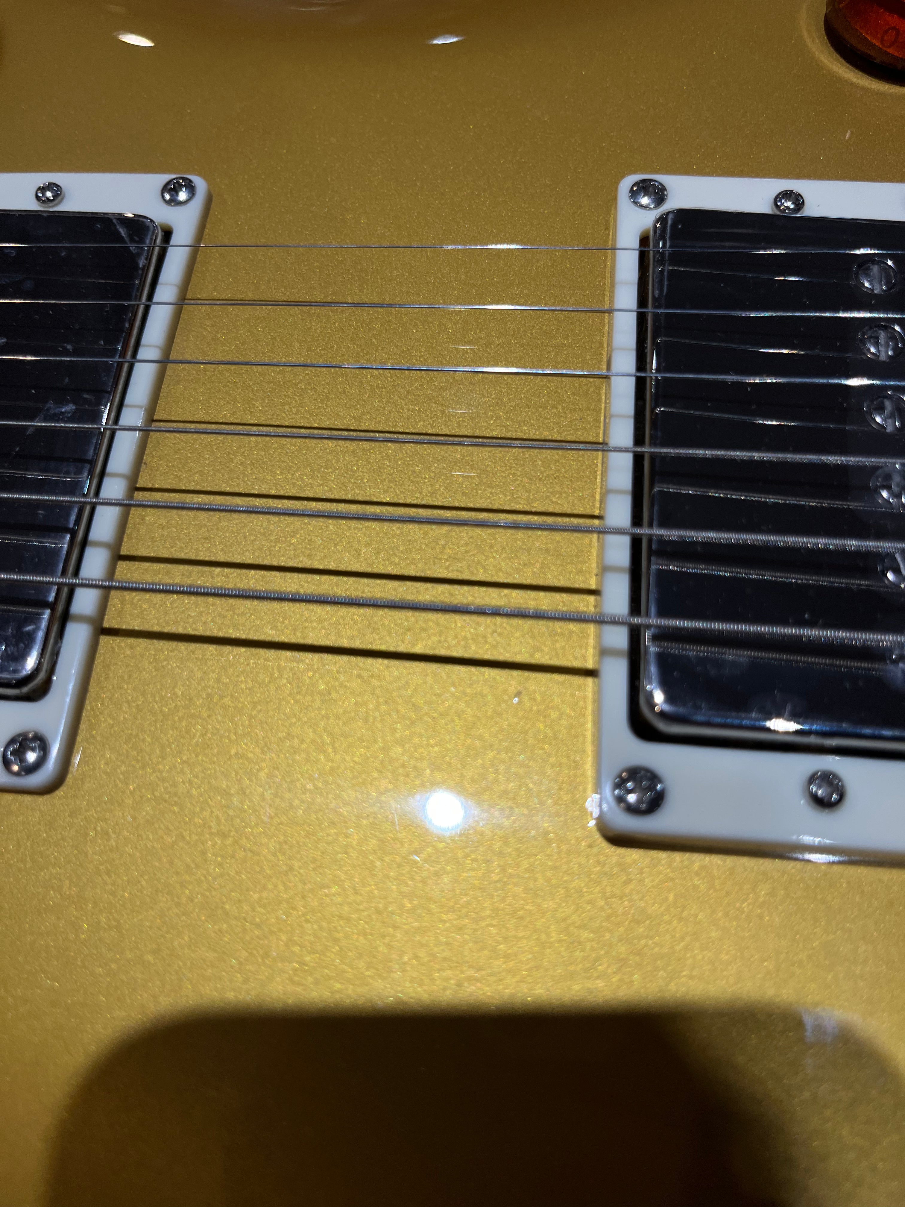 Close-up of a gold electric guitar showing six strings and two chrome pickups with white frames.