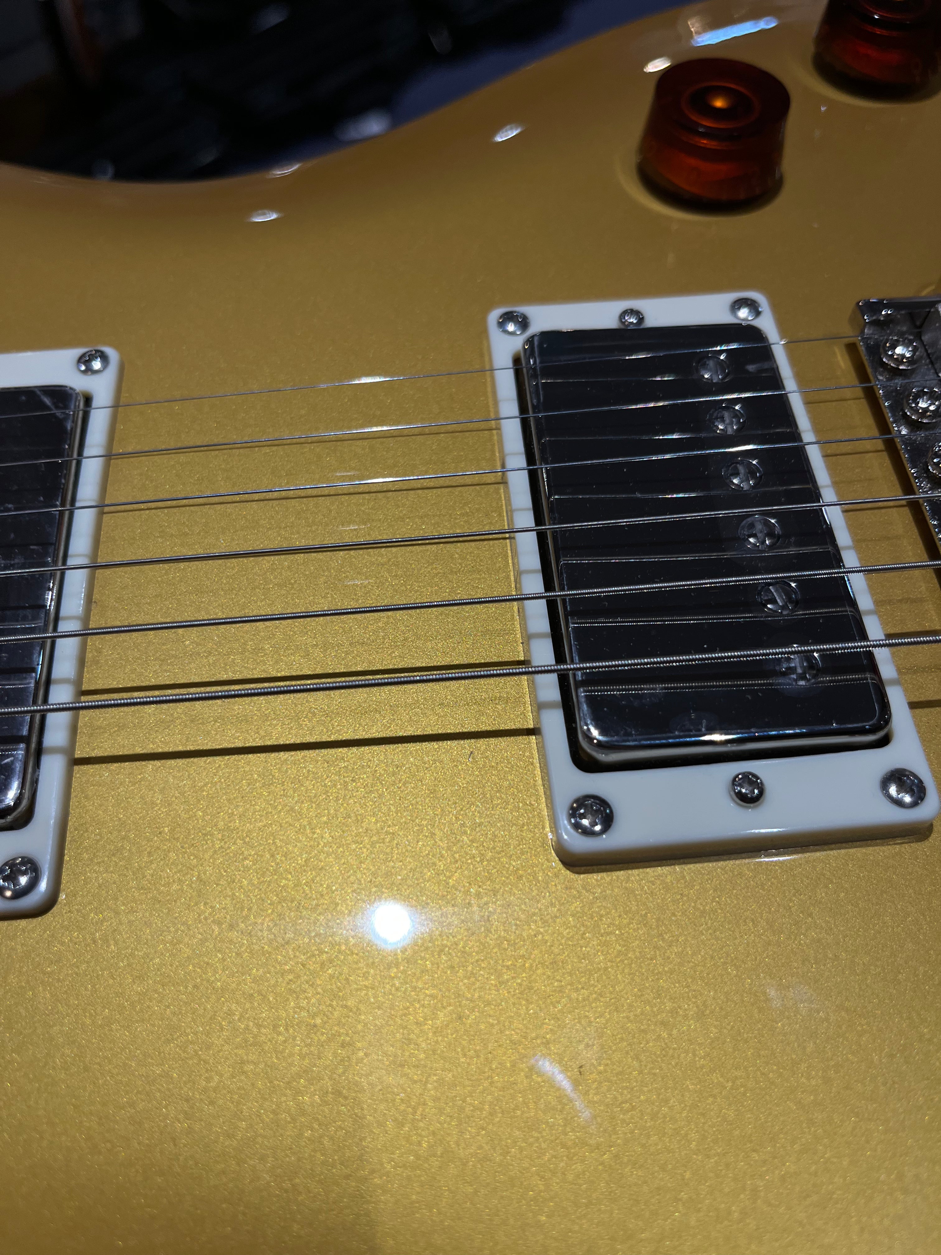 Gold electric guitar body with chrome humbucker pickups, white pickup frames, six metal strings, and an amber-colored control knob.