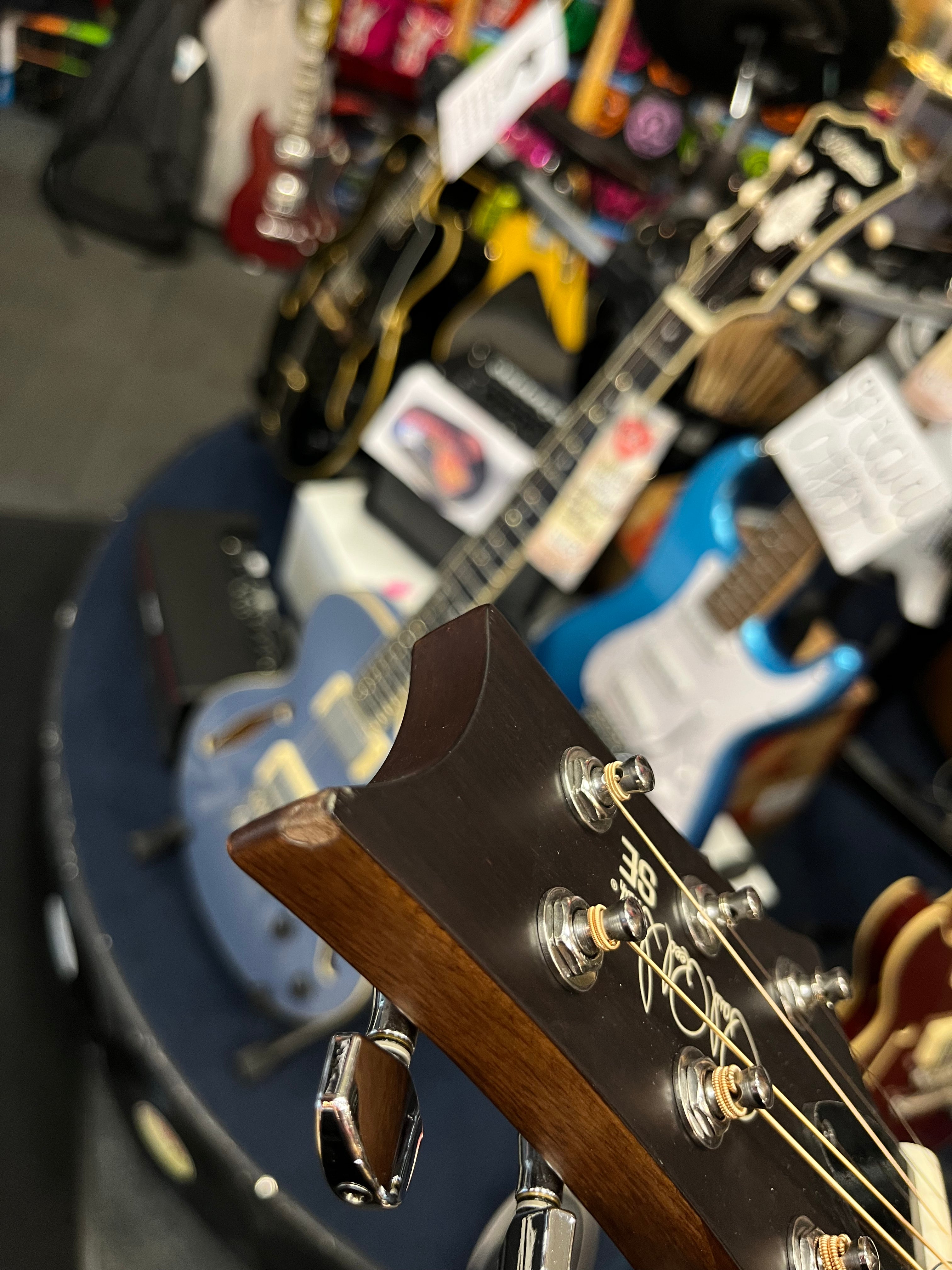 Close-up of an electric guitar headstock with silver tuning pegs, surrounded by various colorful guitars displayed in the background of a music store.