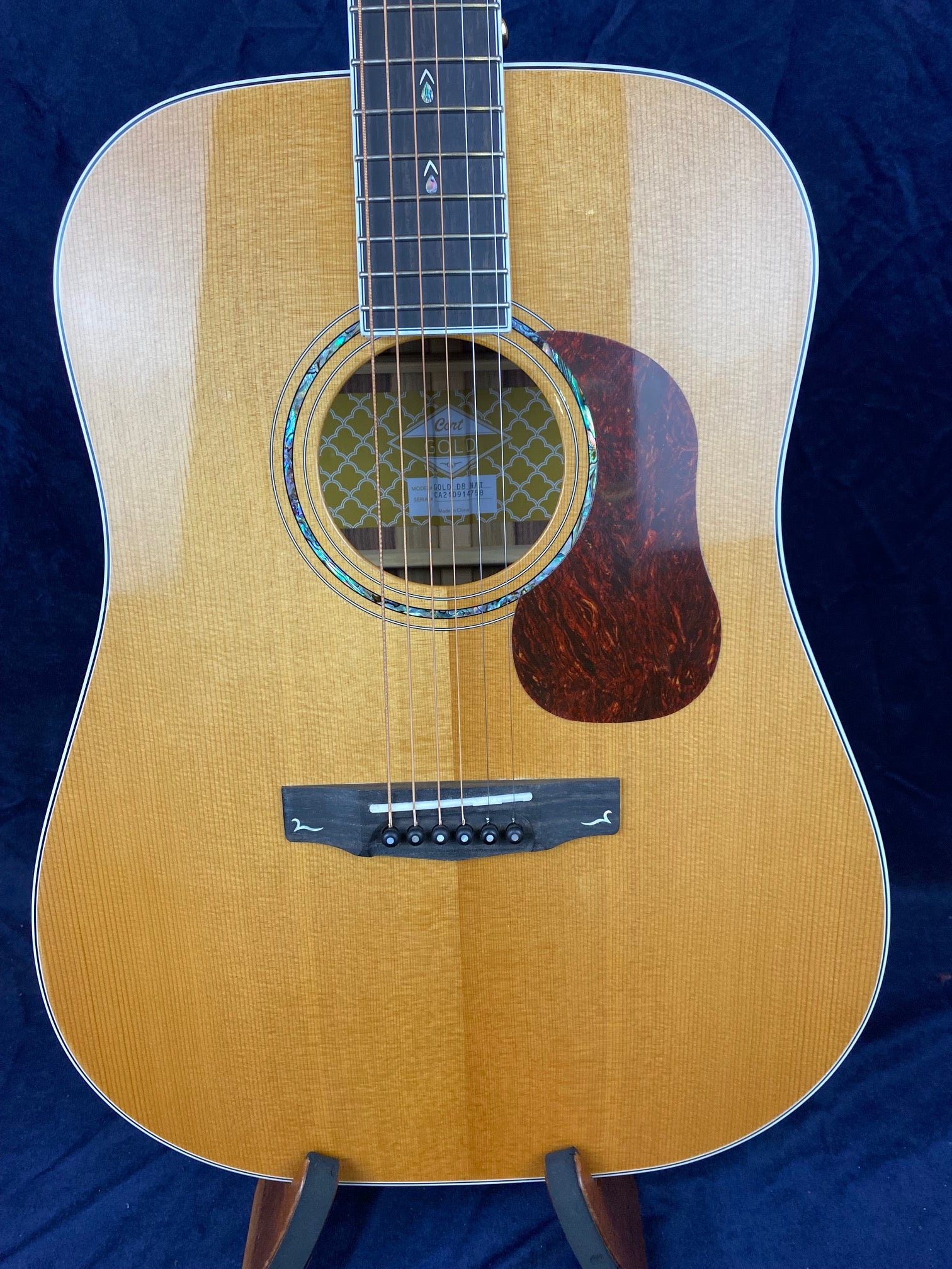 Natural wood finish acoustic guitar with six strings, a decorative soundhole ring, tortoiseshell-style pickguard, and subtle inlays on the fretboard.