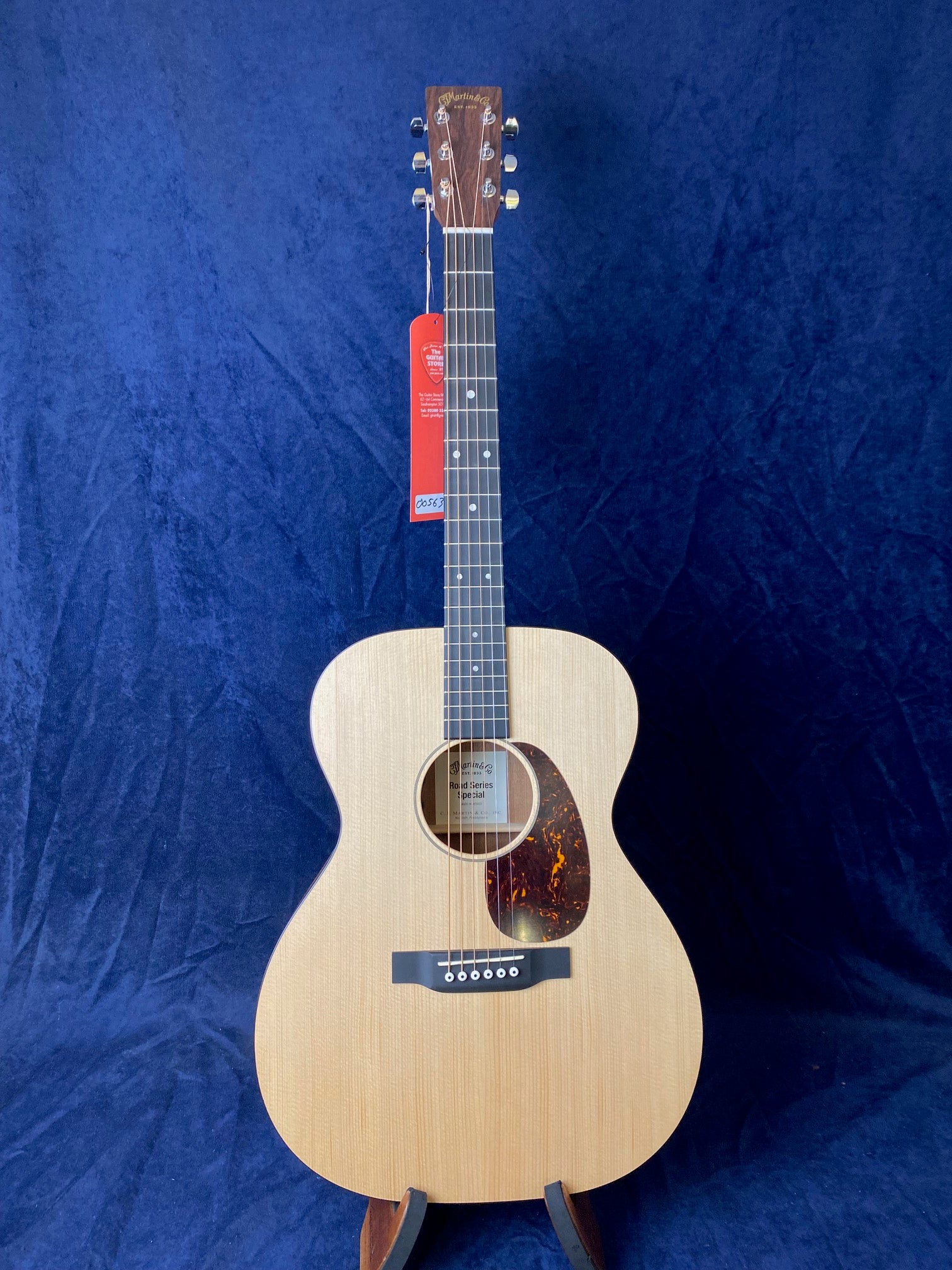 Light wood acoustic guitar with a tortoiseshell-look pickguard, six strings, and a Martin & Co. logo on the headstock, standing against a dark blue background.