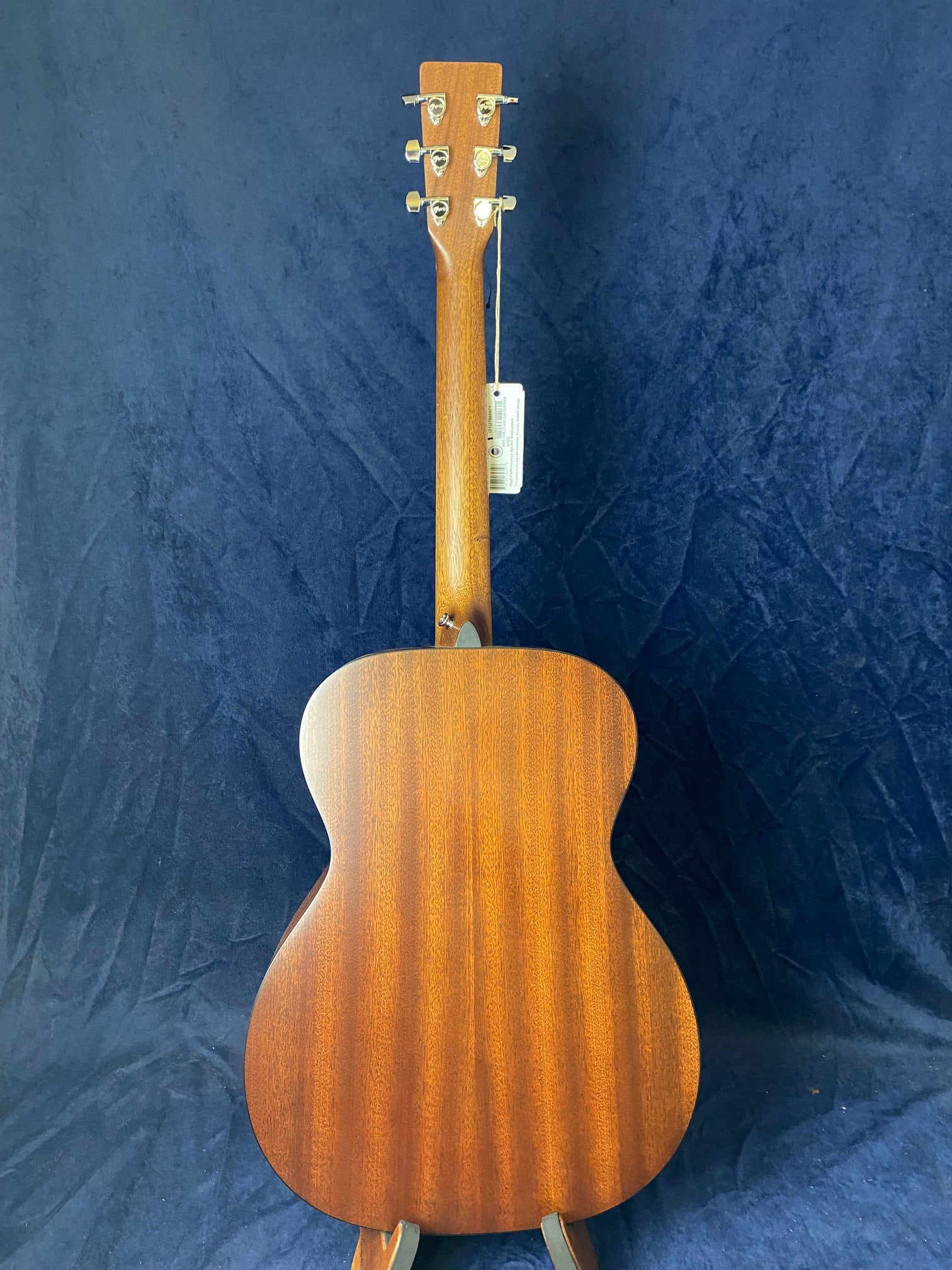 Acoustic guitar shown from the back, with a smooth brown wood finish and six tuning pegs on the headstock.