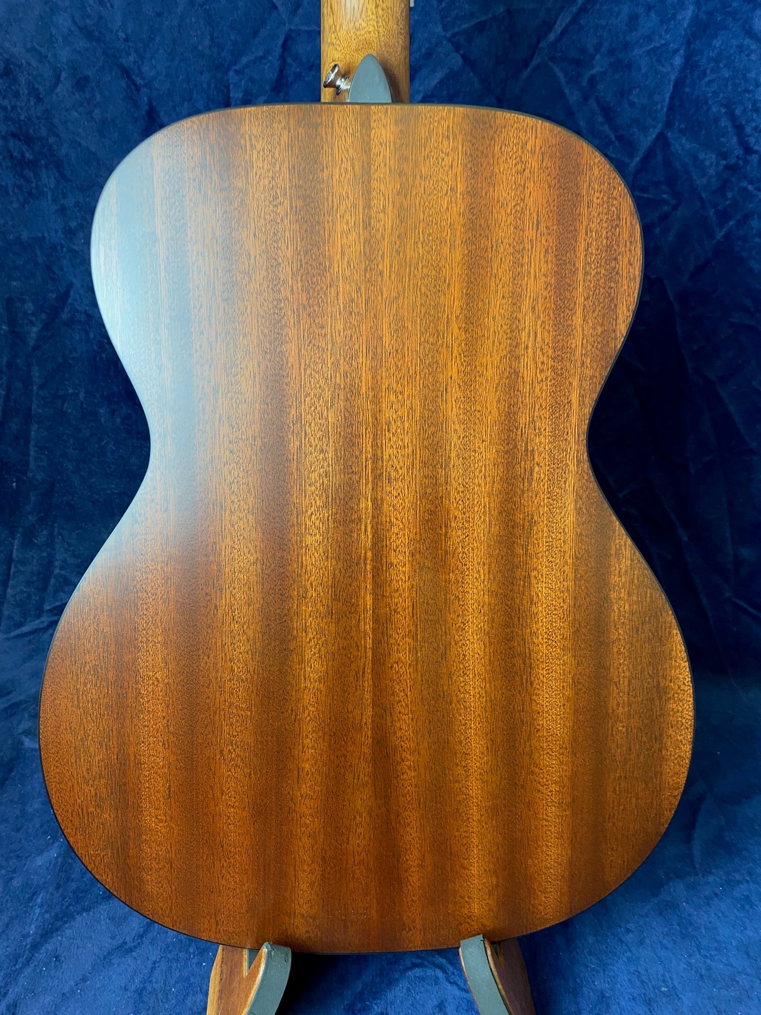 Back view of an acoustic guitar, showing a smooth, rich brown wood grain finish with a curved body and no visible scratches or decorations.
