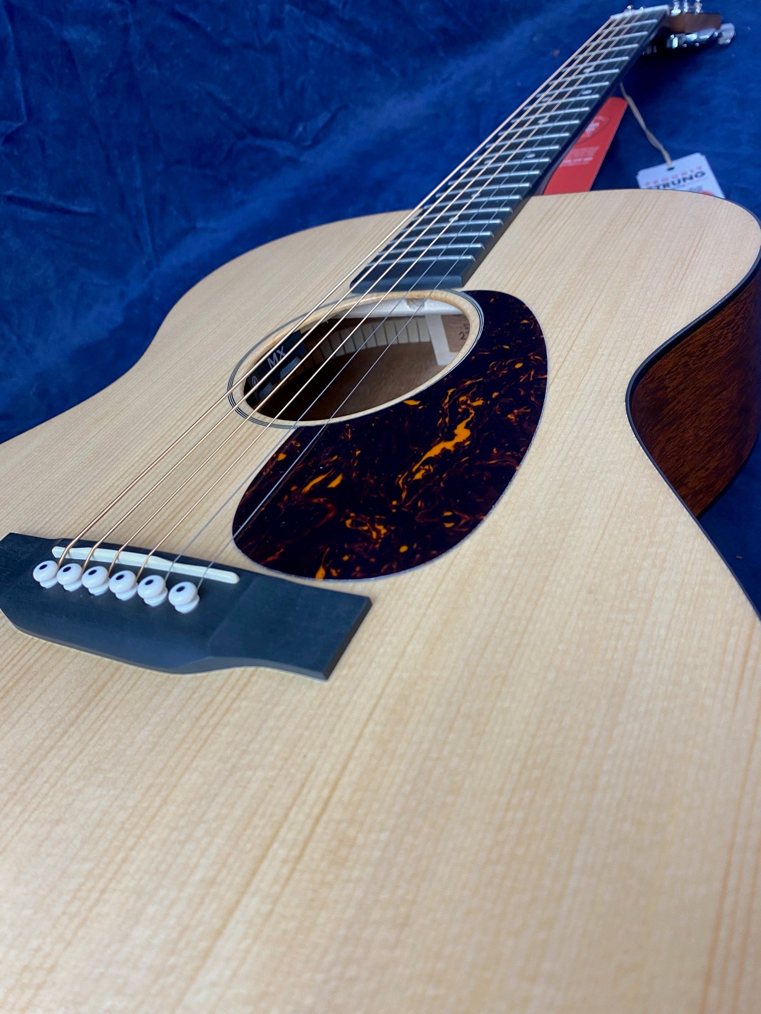 Light wood acoustic guitar with six strings, dark tortoiseshell-pattern pickguard, and white bridge pins, angled on a rich blue background.