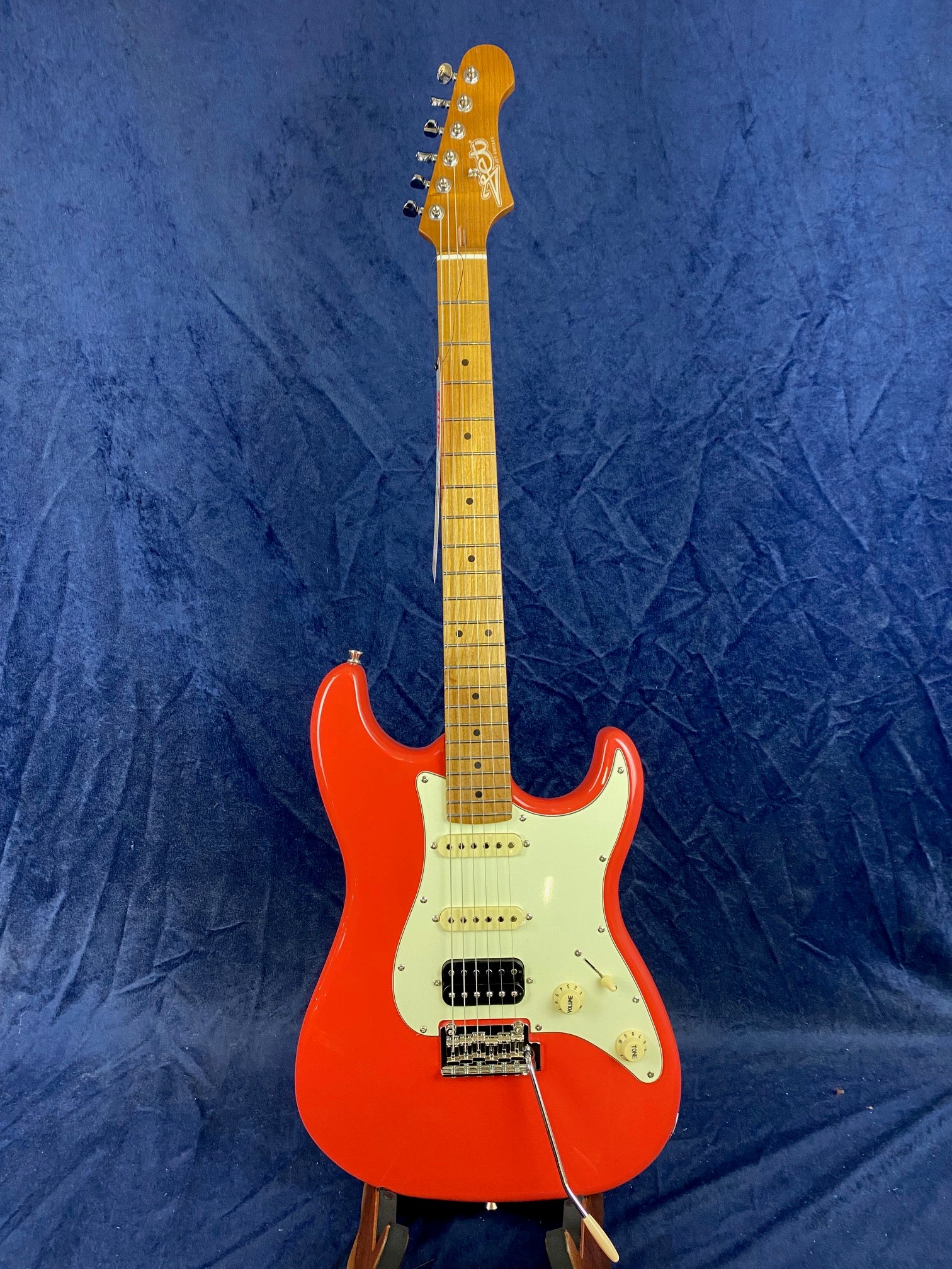 Red electric guitar with a white pickguard, three pickups, and a maple neck, standing upright against a dark blue background.