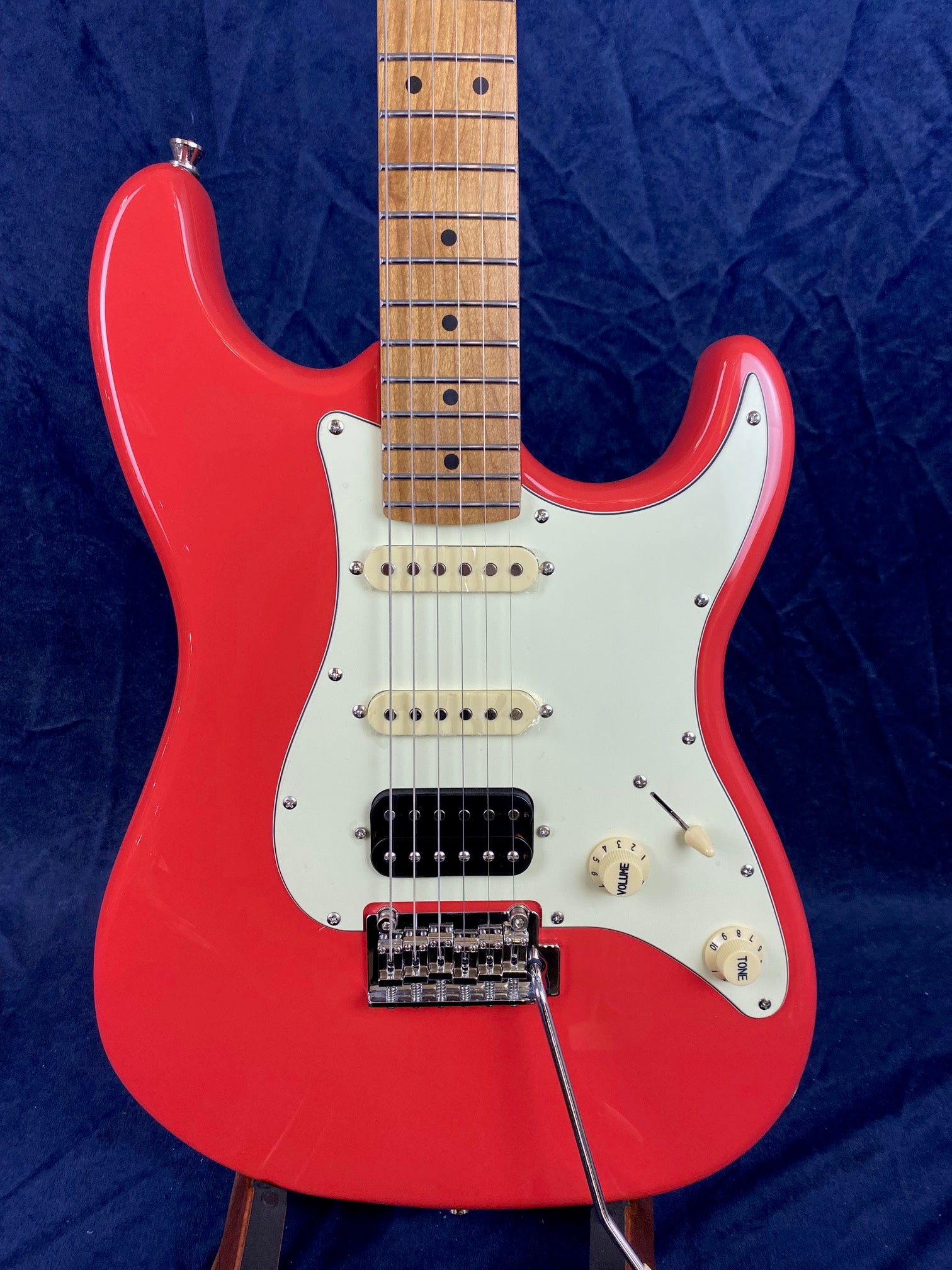 Red electric guitar with a white pickguard, three knobs, and a bridge with a tremolo arm. Maple fretboard with dot inlays.
