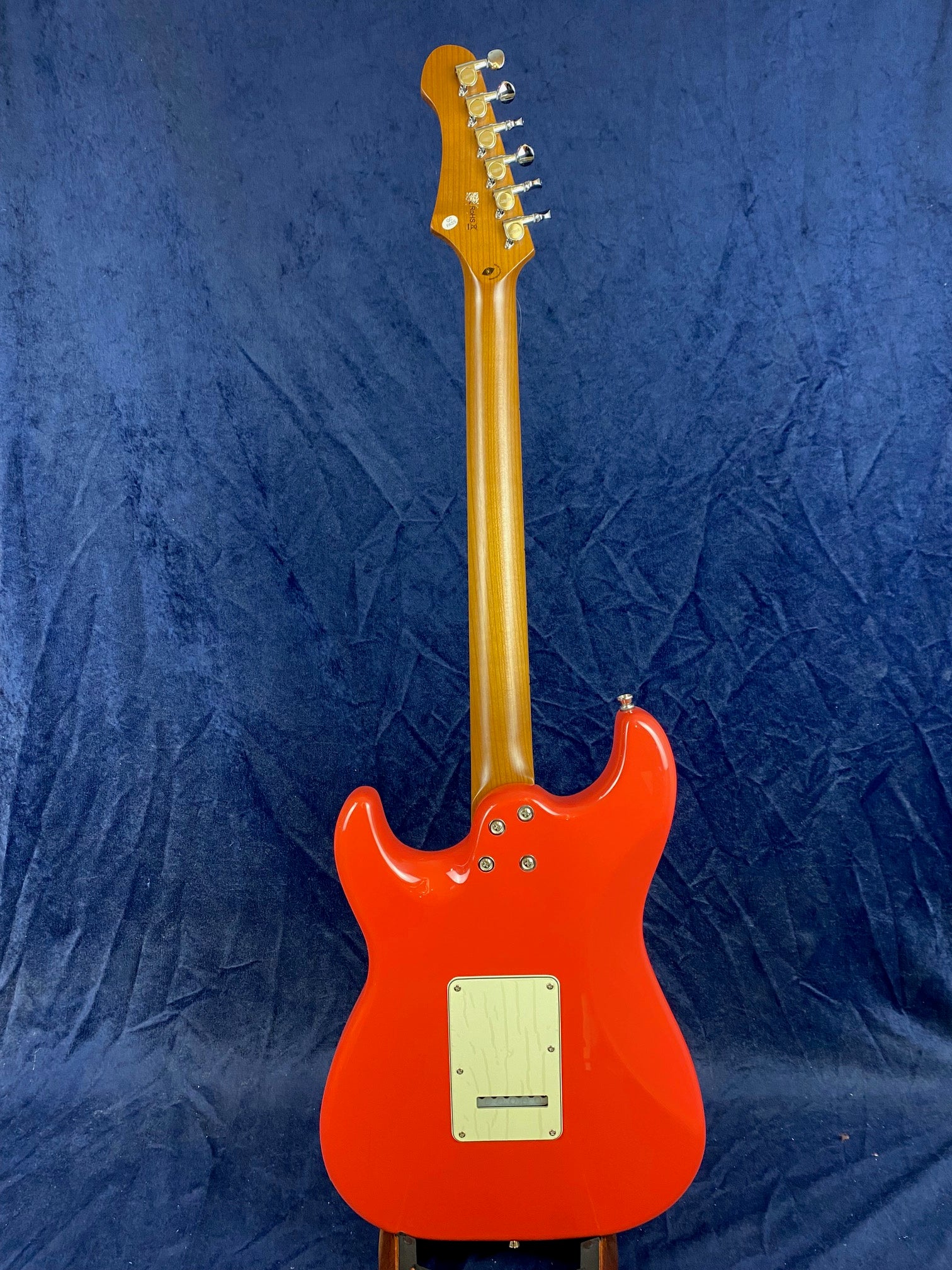 Red electric guitar shown from the back, light wood neck, chrome tuning pegs, white backplate, set against a blue textured background.