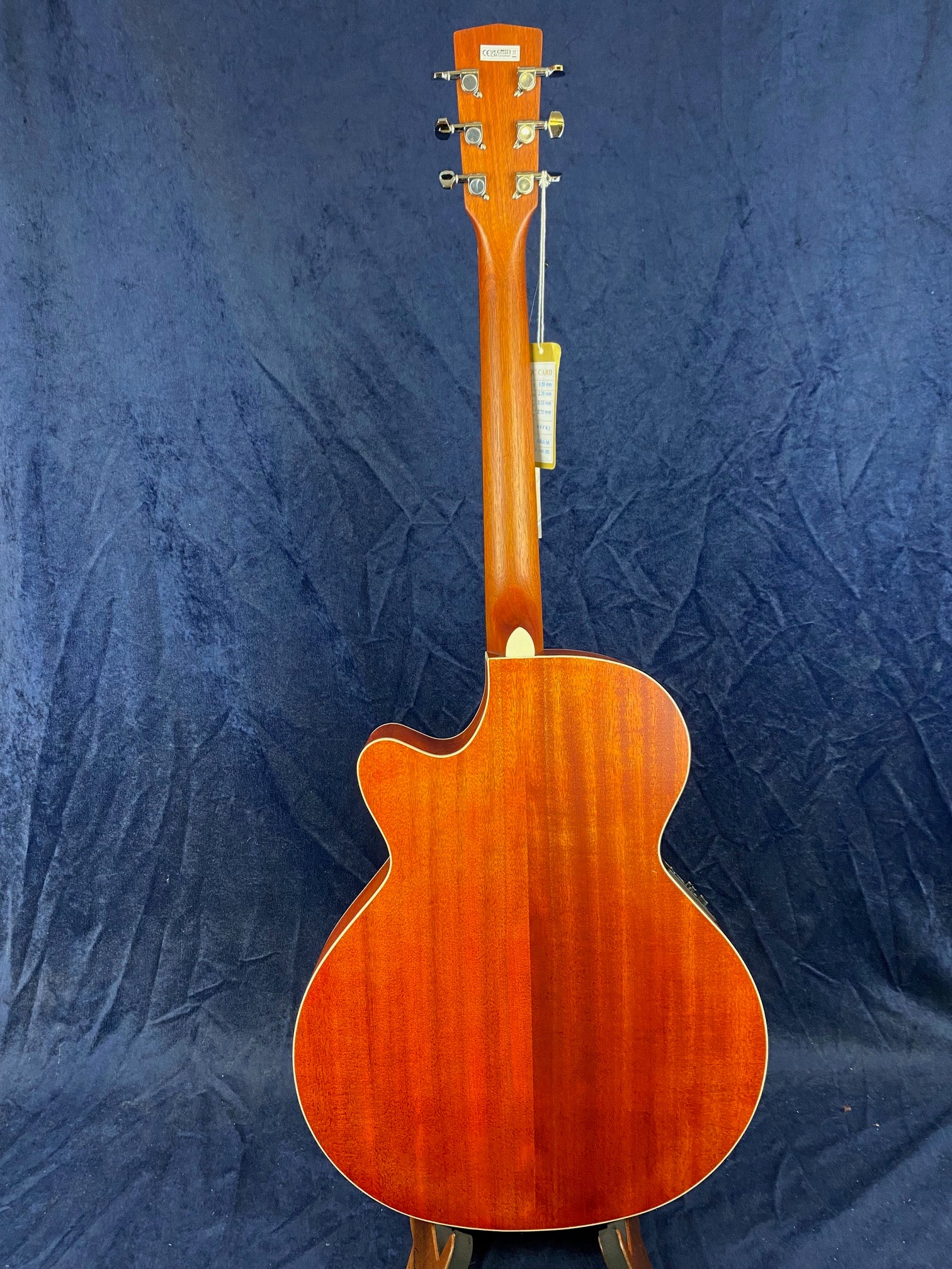 Acoustic guitar shown from the back, featuring a glossy reddish-brown wood finish with a single cutaway and six tuning pegs on the headstock.
