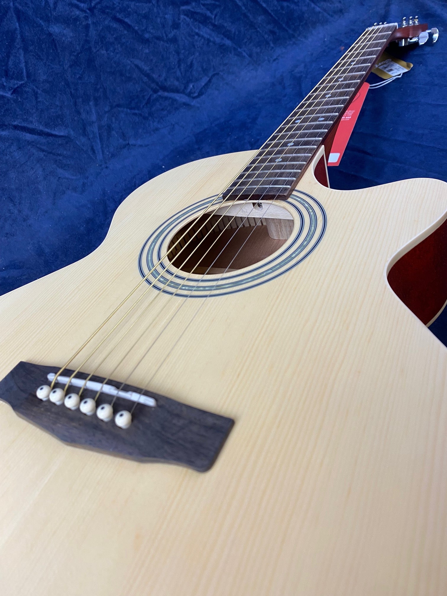 Light wood acoustic guitar with six strings, a round sound hole, dark bridge, and cutaway body against a dark blue background.