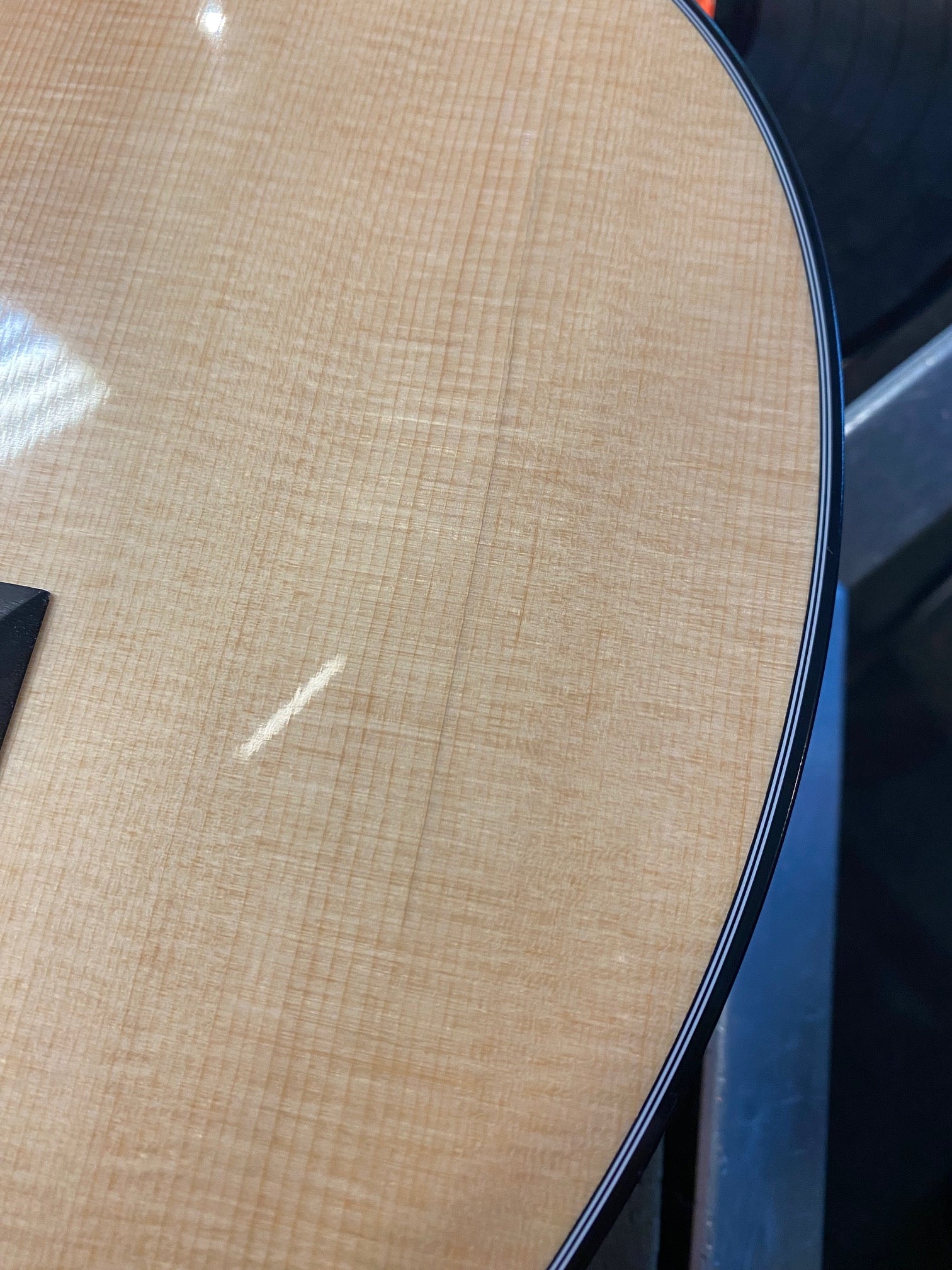 Close-up of an acoustic guitar’s light wood body with subtle vertical grain and dark edge binding visible.