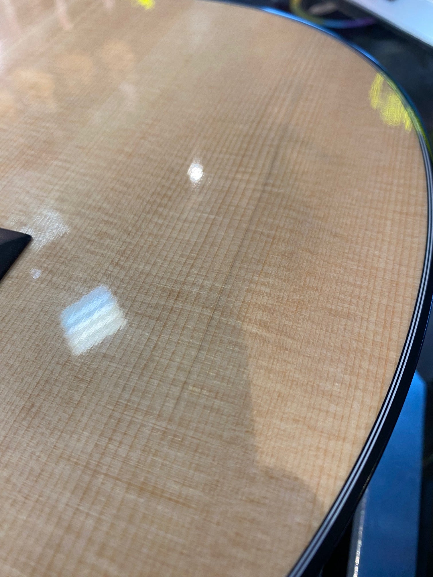 Close-up of an acoustic guitar’s glossy, light wood top with fine vertical grain lines and a black-edged binding.