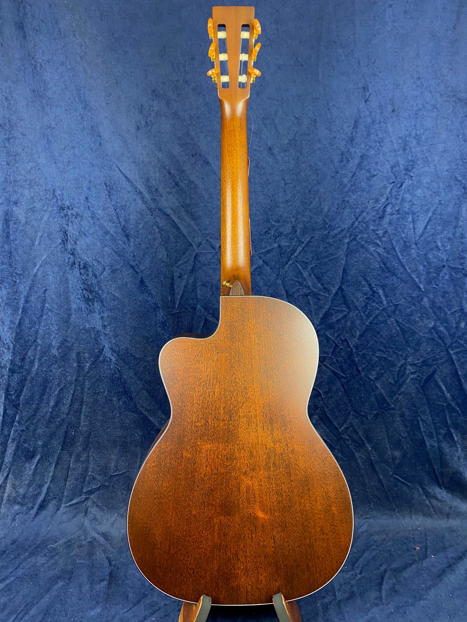 Back view of an acoustic guitar with a rich brown wood finish and a cutaway body shape, set against a dark blue background.