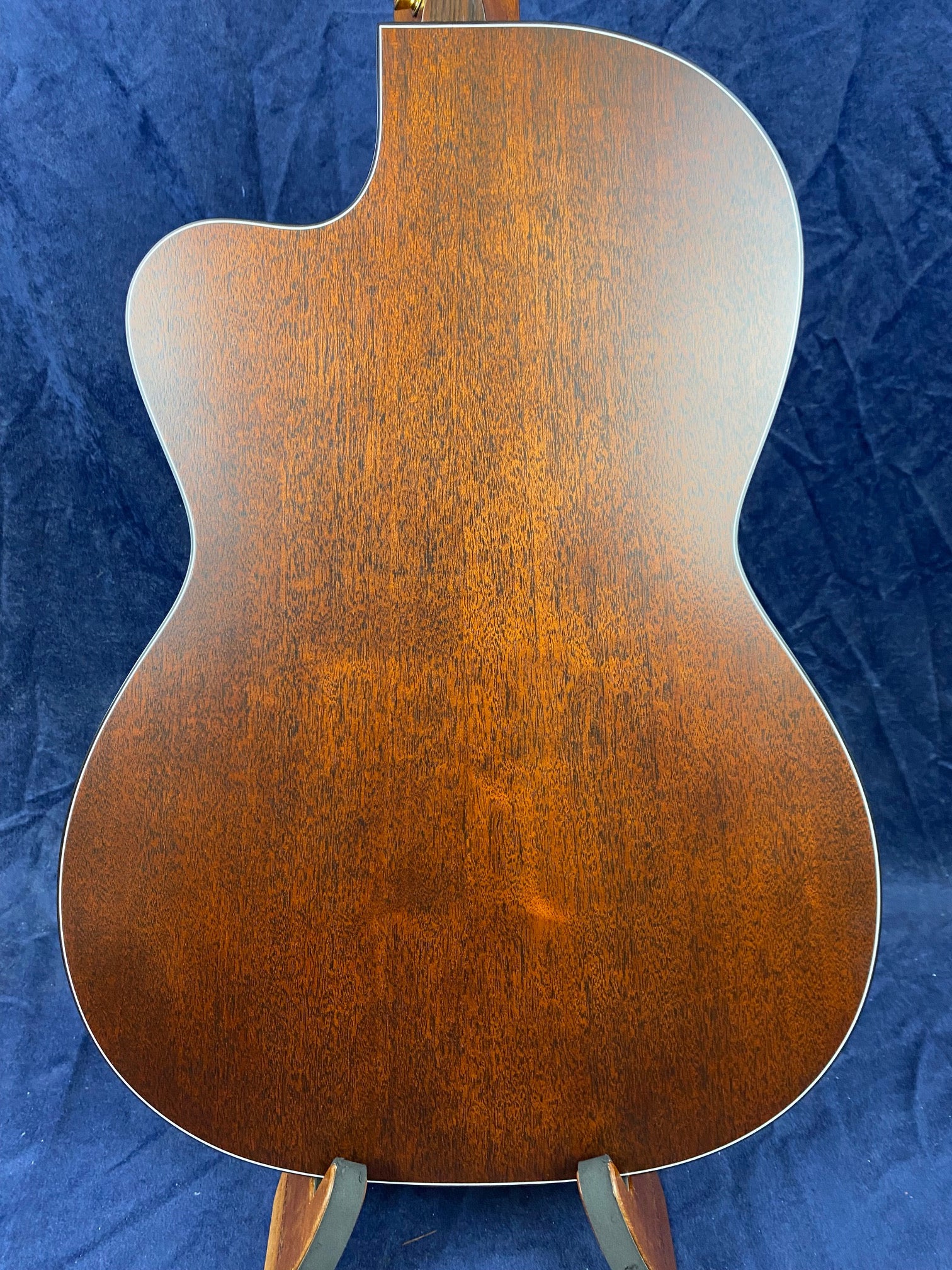 The back of an acoustic guitar shows smooth, rich brown wood with a natural grain pattern and a single cutaway at the top left.