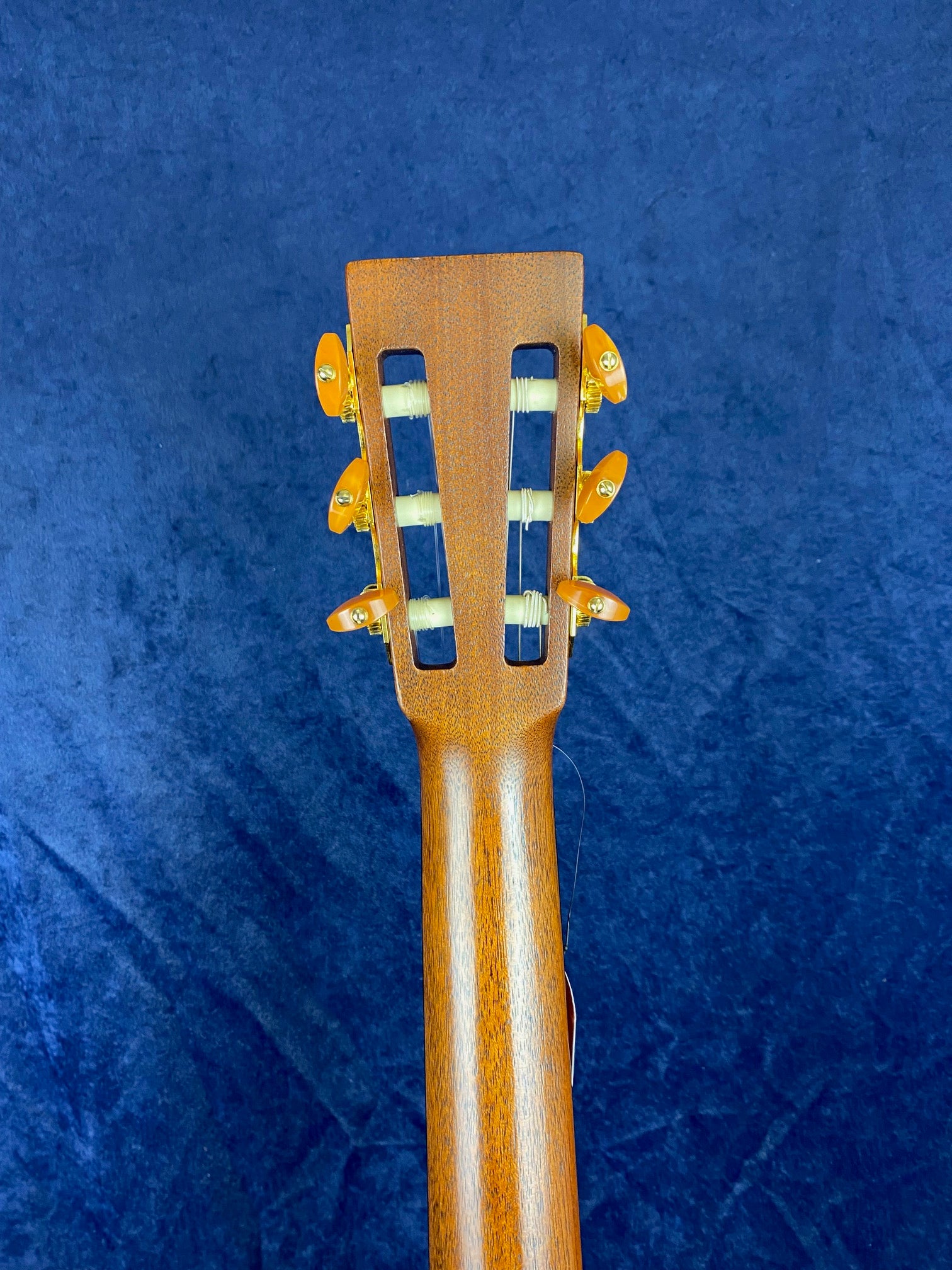Back of an acoustic guitar headstock showing six gold tuning pegs and two rectangular slots in the wood, with a smooth brown neck below.