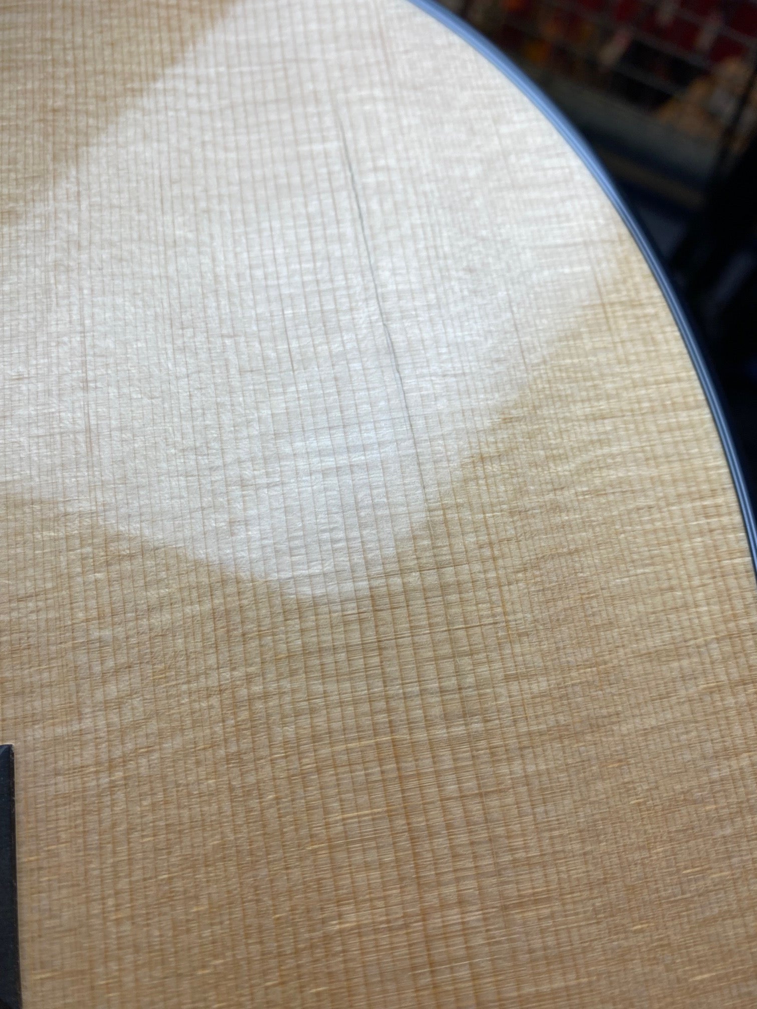 Light-colored acoustic guitar top with a subtle wood grain pattern and a glossy finish, showing a curved black edge binding in the upper right.