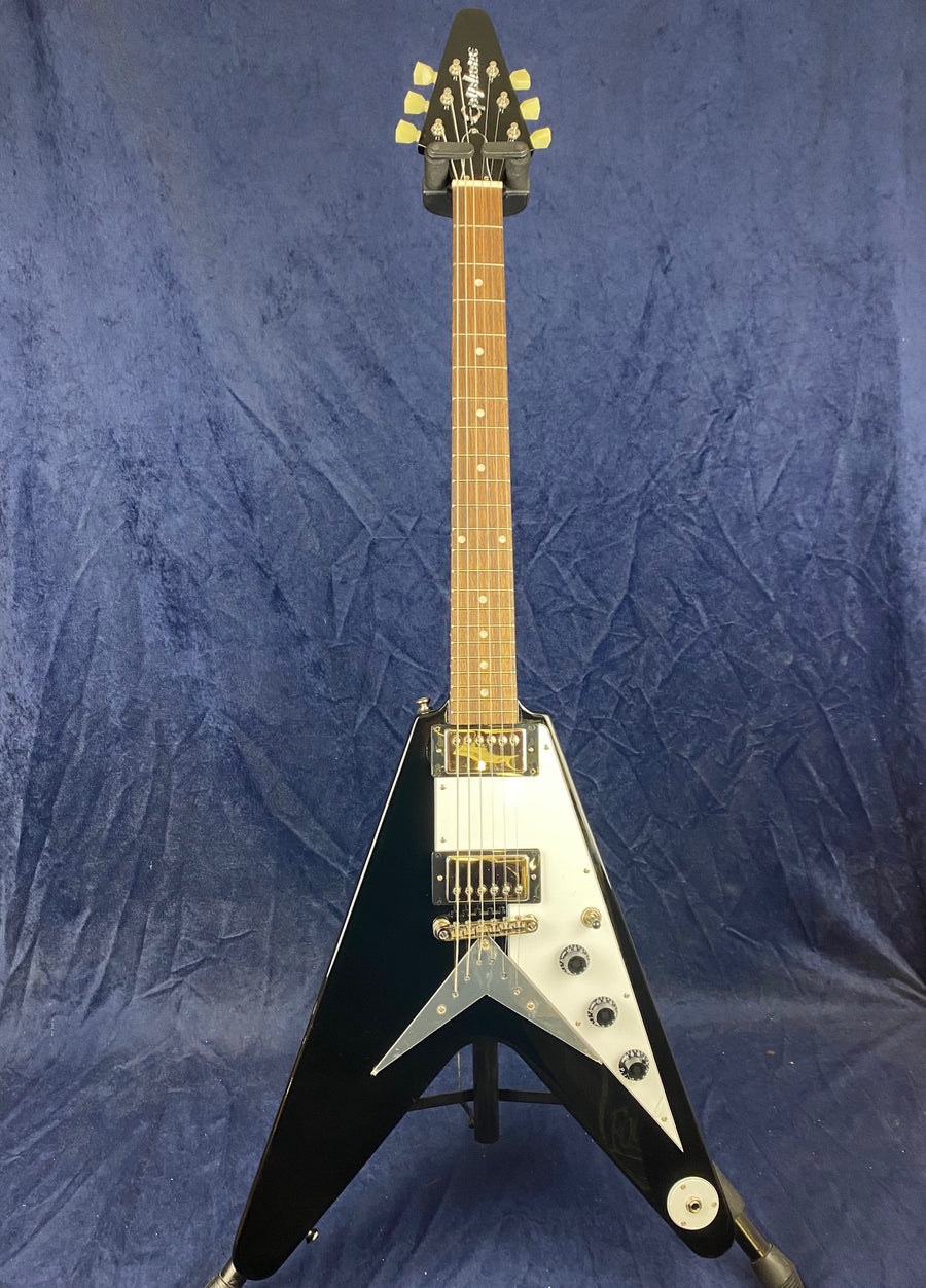 Black electric guitar with a V-shaped body, white pickguard, two humbucker pickups, four control knobs, and a natural wood neck.