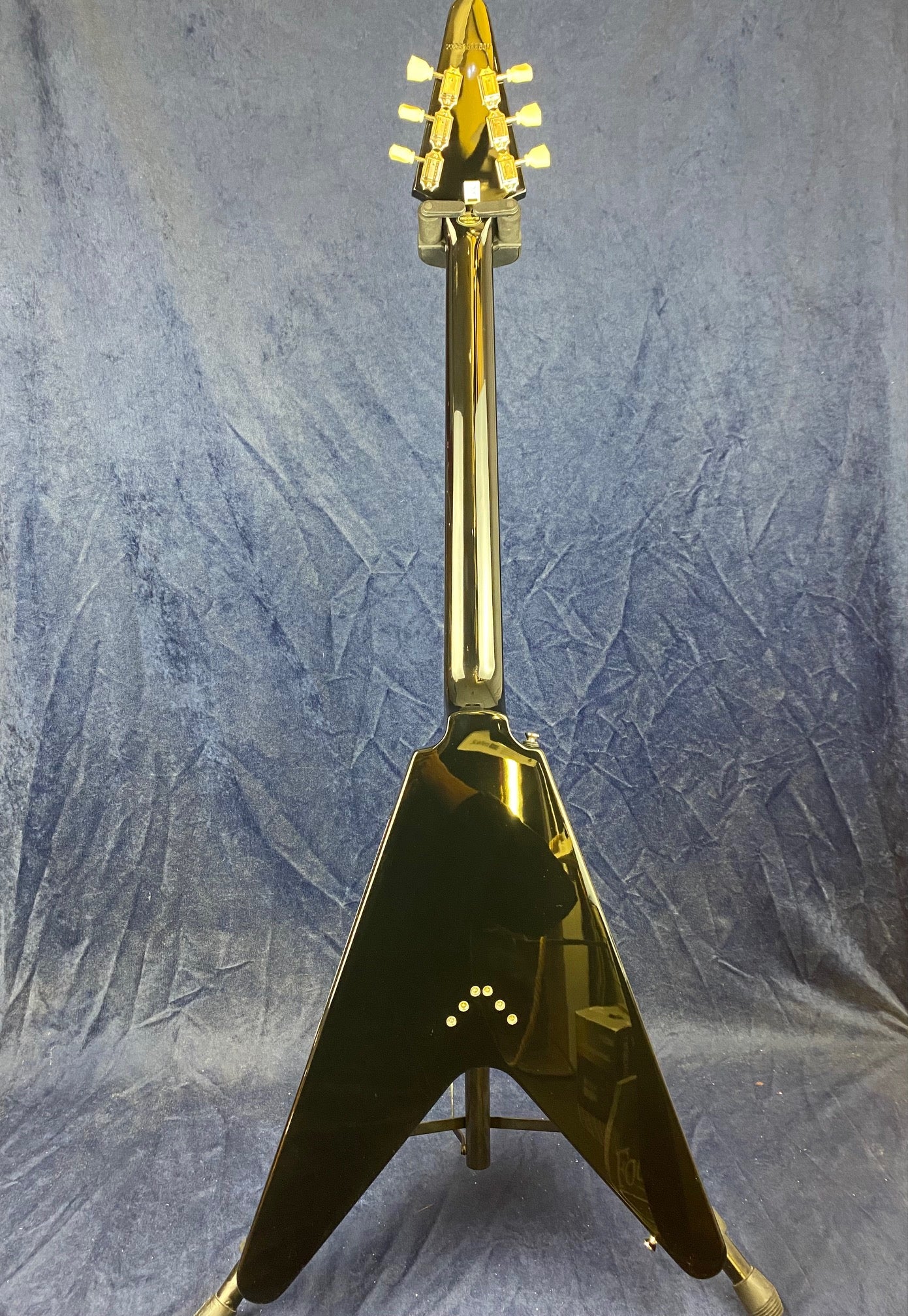 Black V-shaped electric guitar shown from the back, gold tuning pegs, with a row of small circular inlays near the bottom center of the body.