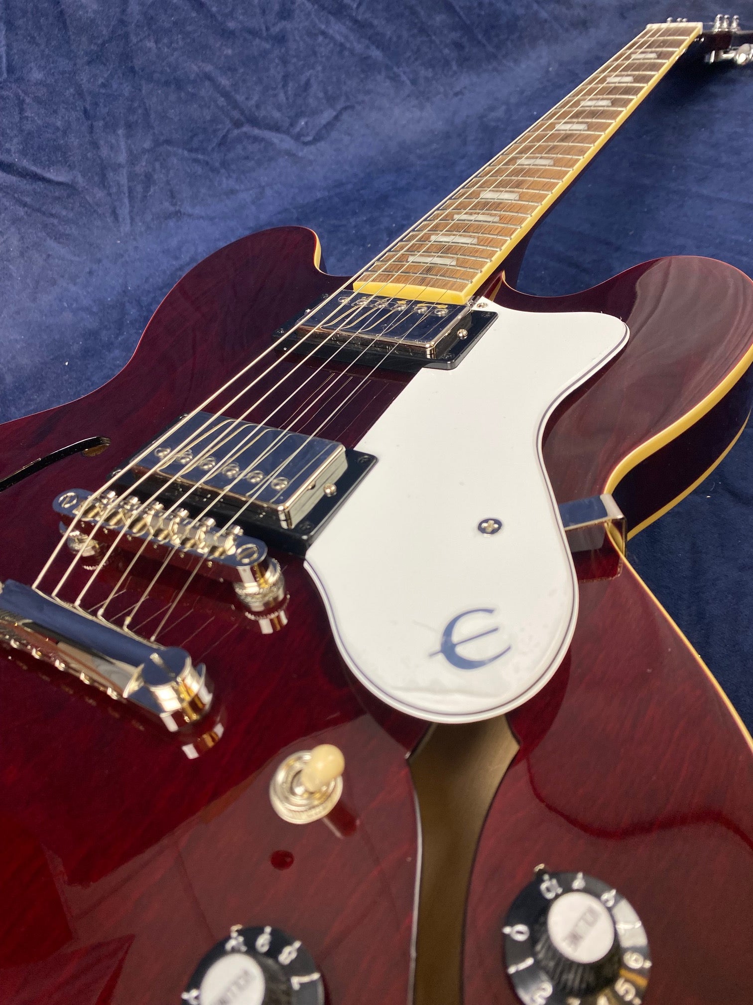Cherry red electric guitar with a semi-hollow body, white pickguard, two humbucker pickups, and chrome hardware on a dark blue background.