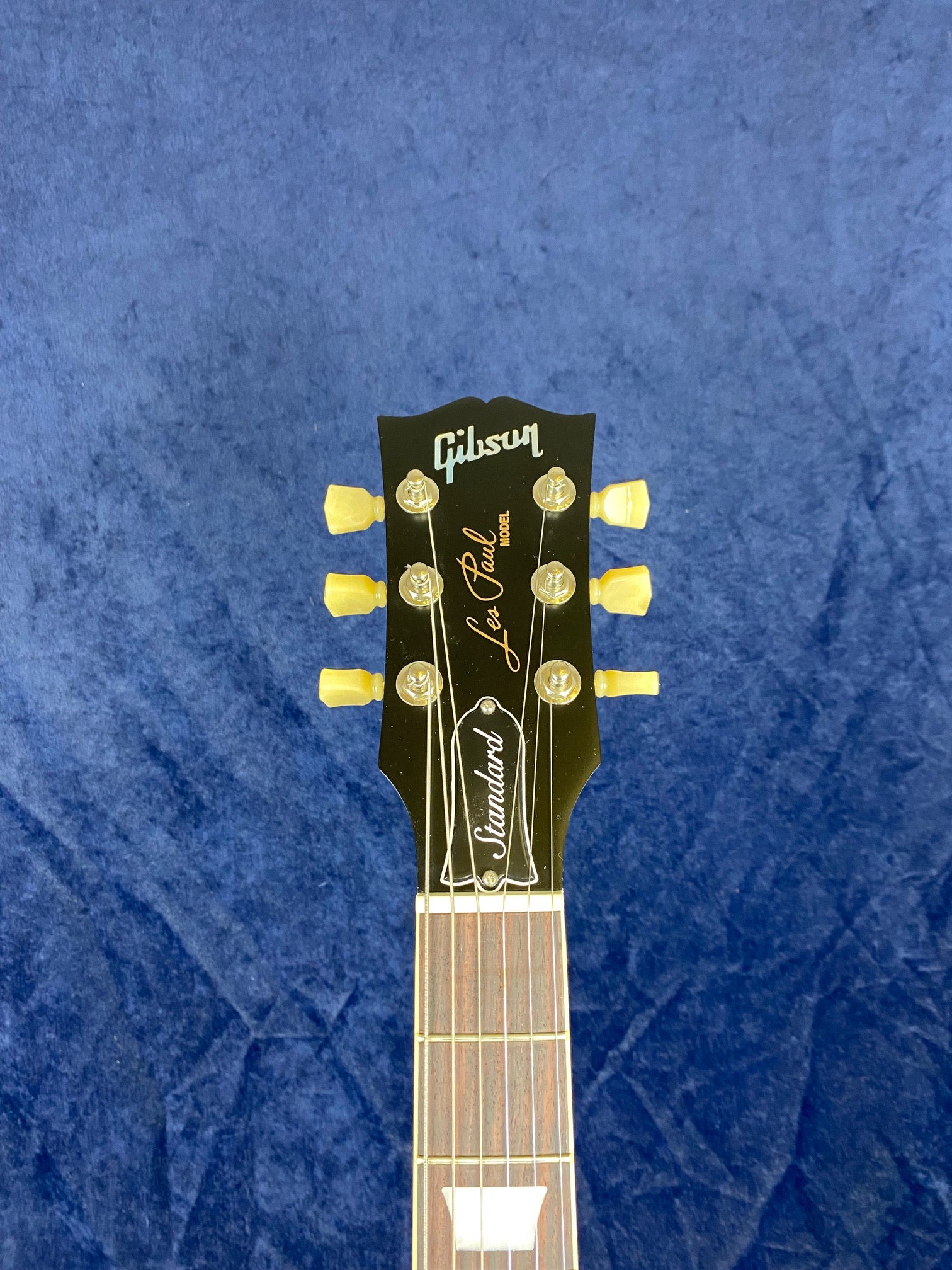 Gibson Les Paul electric guitar headstock with gold tuning pegs, truss rod cover labeled "Standard," and signature logo on a blue background.