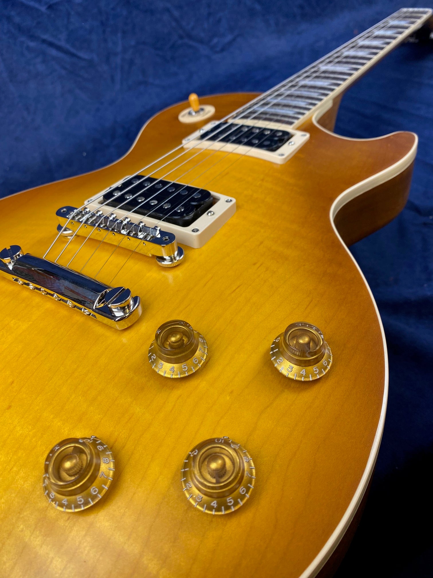 Sunburst electric guitar with two humbucker pickups, four gold control knobs, a chrome bridge, cream trim, and a dark blue background.