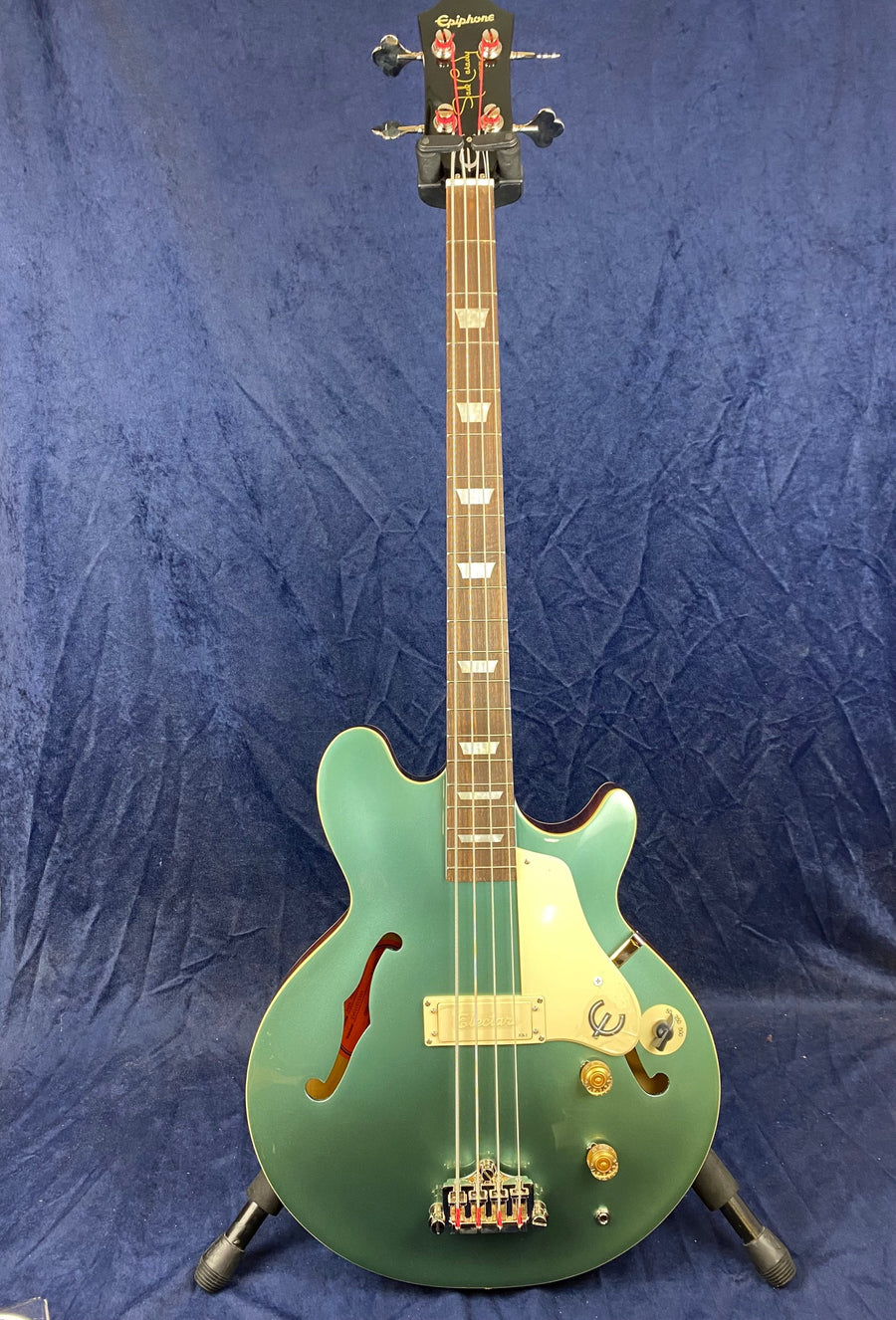 Green Epiphone semi-hollow body bass guitar with white pickguard, f-holes, four strings, gold knobs, and triangle inlays on a wooden neck.