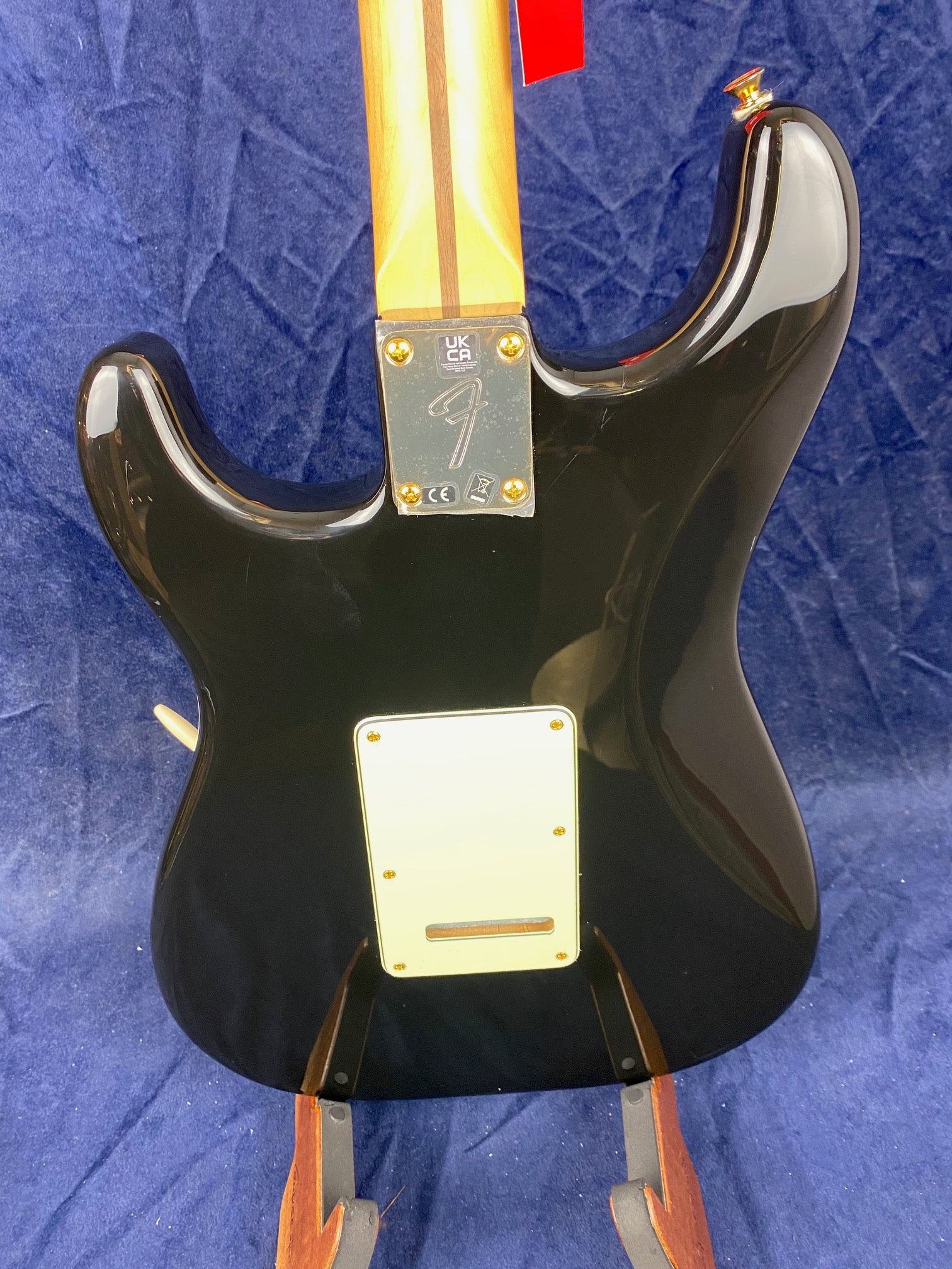 Black electric guitar rear view, showing a maple neck with a dark stripe, a metal neck plate with logos, and a cream-colored back plate.